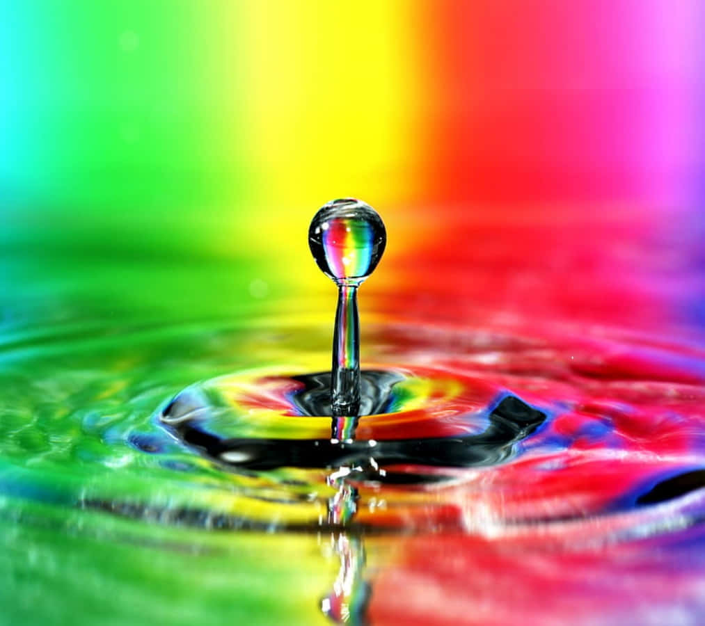 Water Drop 桌布 壁紙 — 一滴完美水珠懸浮在漣漪表面之上，反射出鮮豔的彩虹漸變背景。