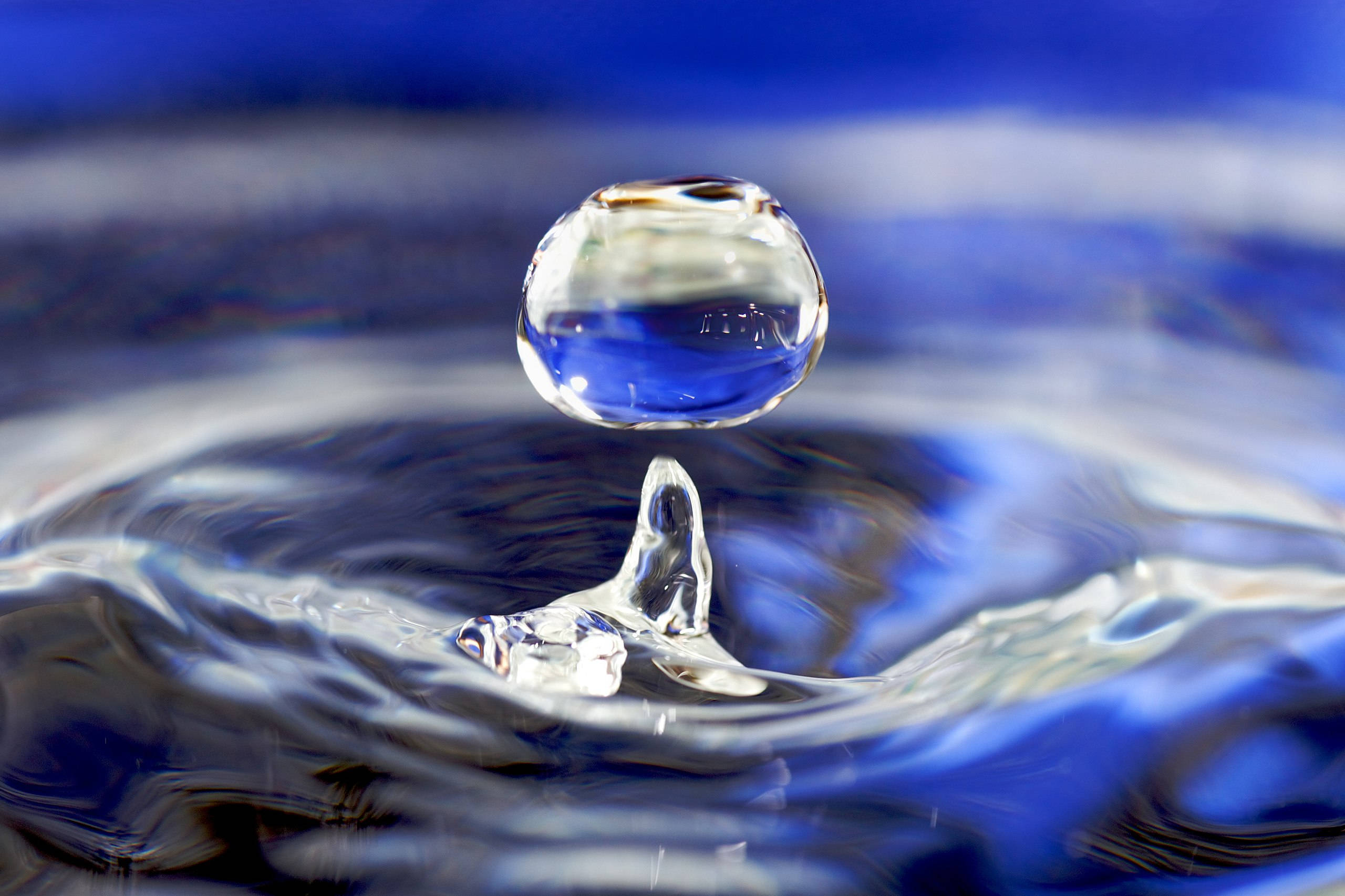 Water Drop 桌布 壁紙 — 一滴完美的水珠懸浮在漣漪表面之上，捕捉深藍色的倒影和銳利的光折射。