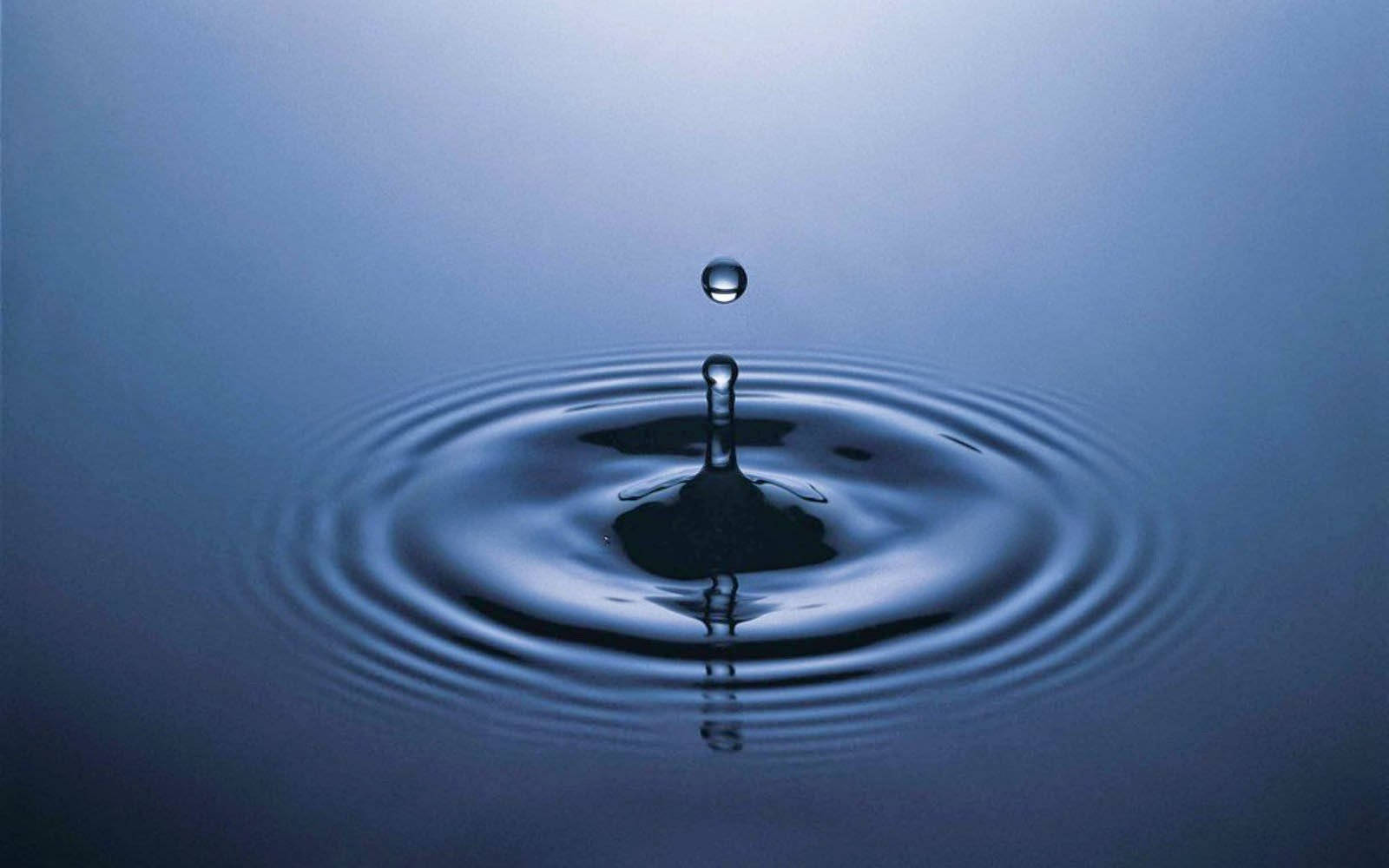 Rippling 桌布 壁紙 — 一滴水懸浮在平靜的藍色水面上，以慢動作創造出完美的同心漣漪。
