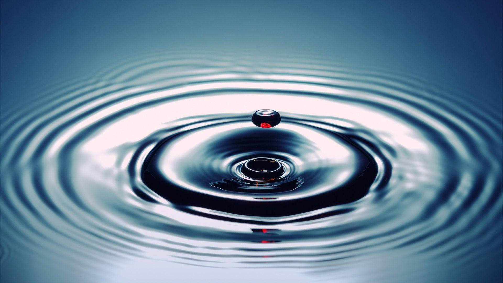 水 桌布 壁紙 — 一滴水懸浮在漣漪的水面上，在冷藍色燈光下形成同心圓環。