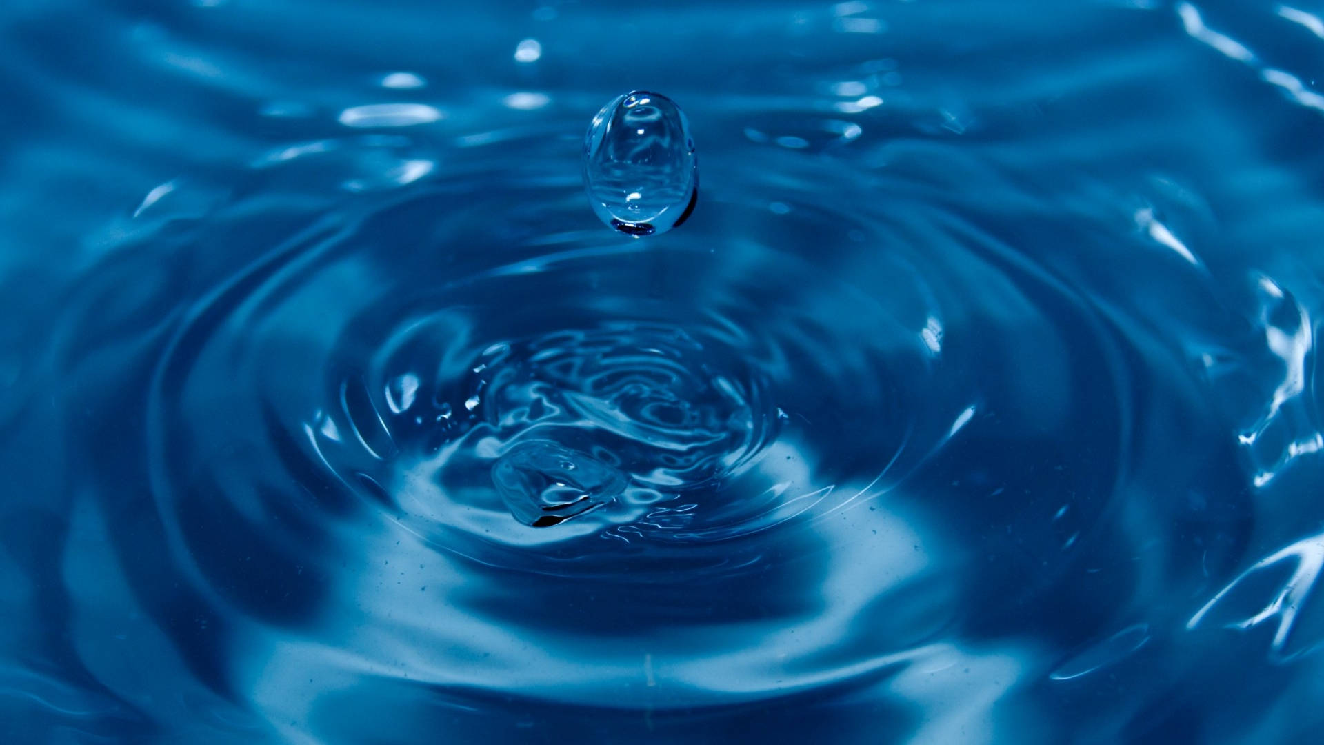 水 桌布 壁紙 — 一滴水懸浮在漣漪的藍色表面上，以慢動作形成同心圓。