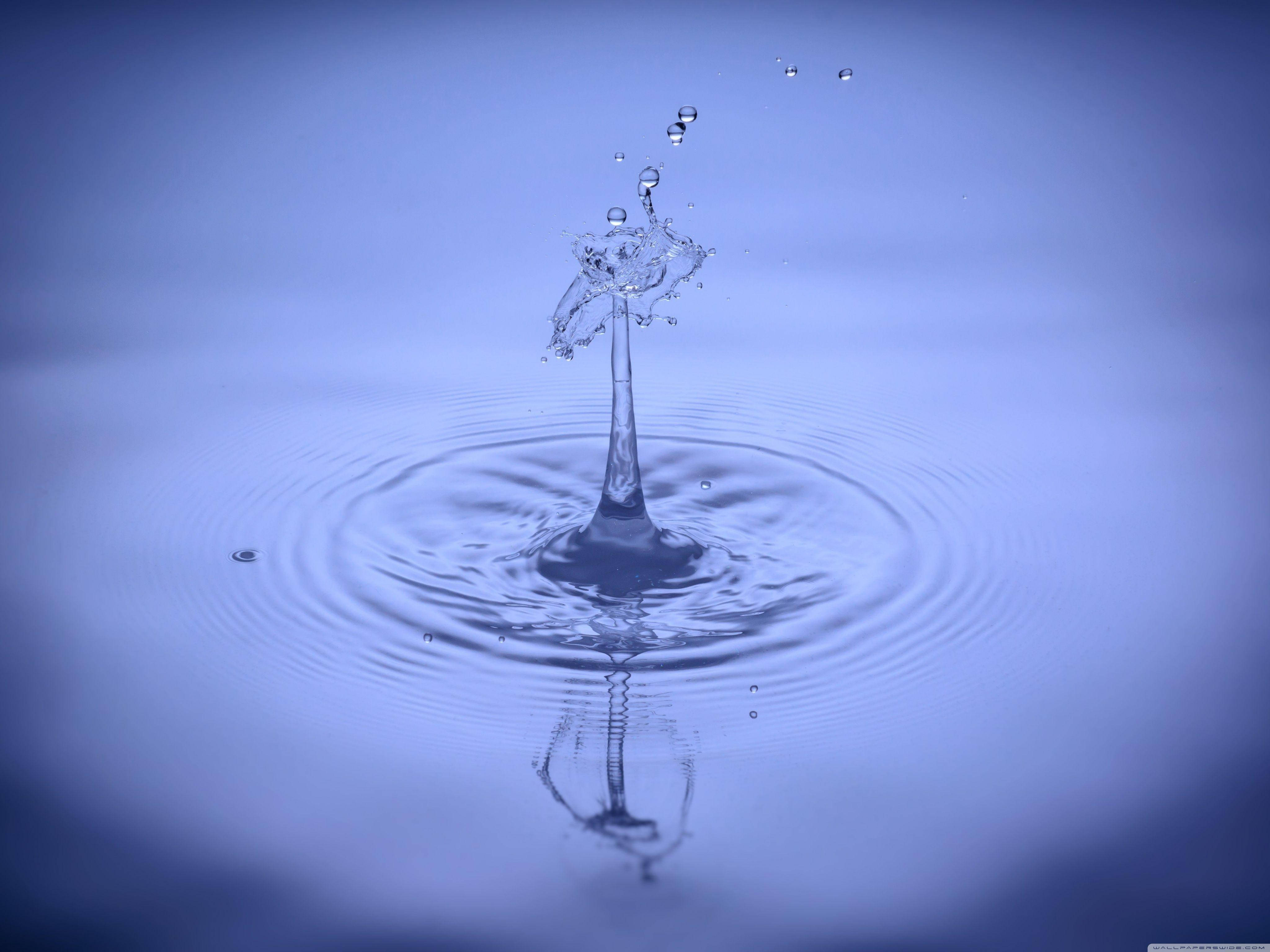 Rippling 桌布 壁紙 — 一滴水珠以慢動作向上飛濺，在平靜的藍色表面上形成完美的同心漣漪。