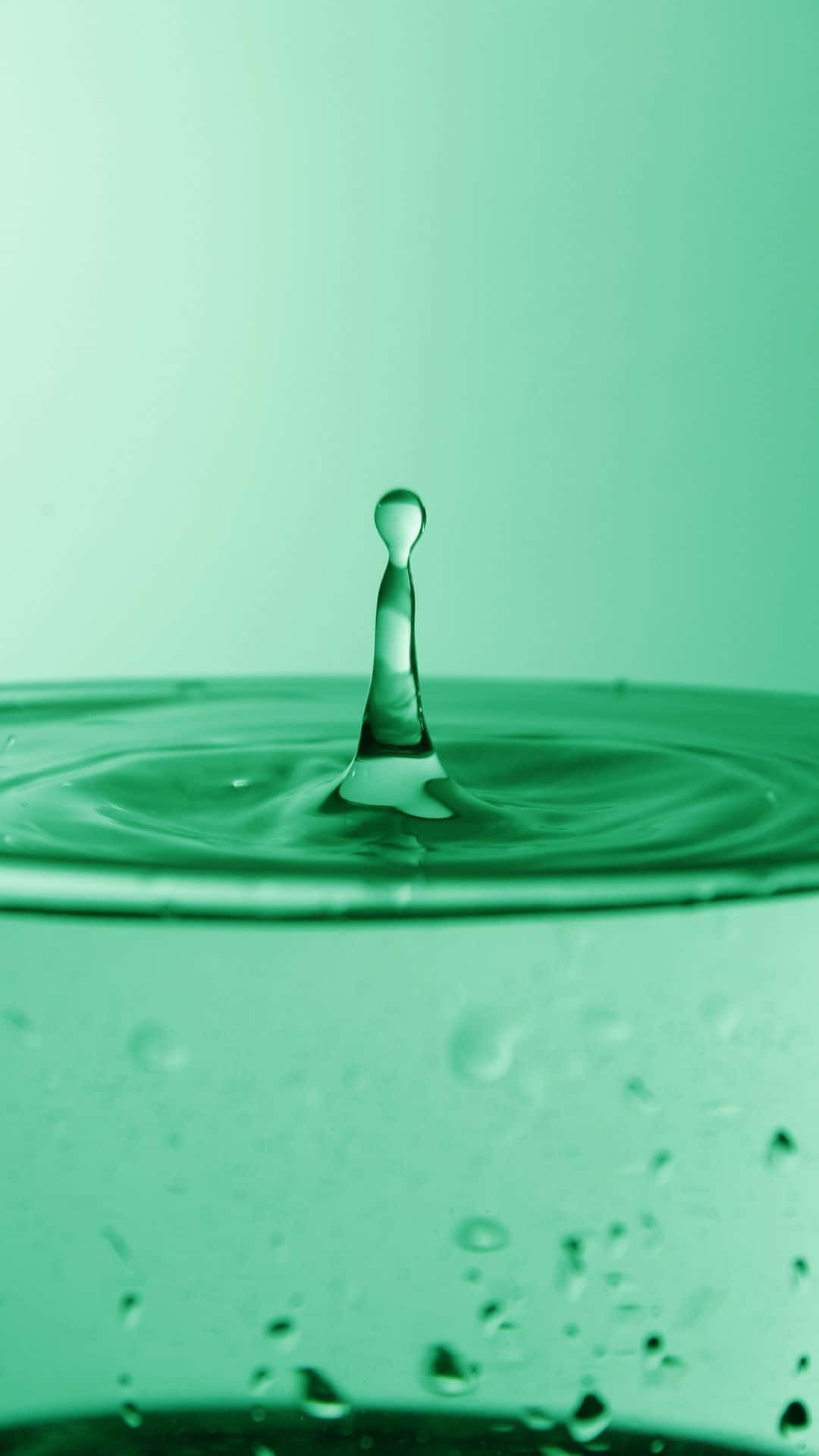 簡約 桌布 壁紙 — 一滴水珠懸浮在半空中，下方是泛起漣漪的綠色水面，形成同心圓。
