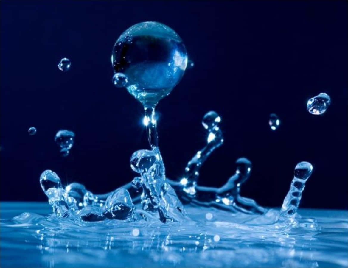 Water Drop 桌布 壁紙 — 一滴水珠懸浮在泛起漣漪的水面上方，伴隨著閃爍的水花，背景是深藍色。
