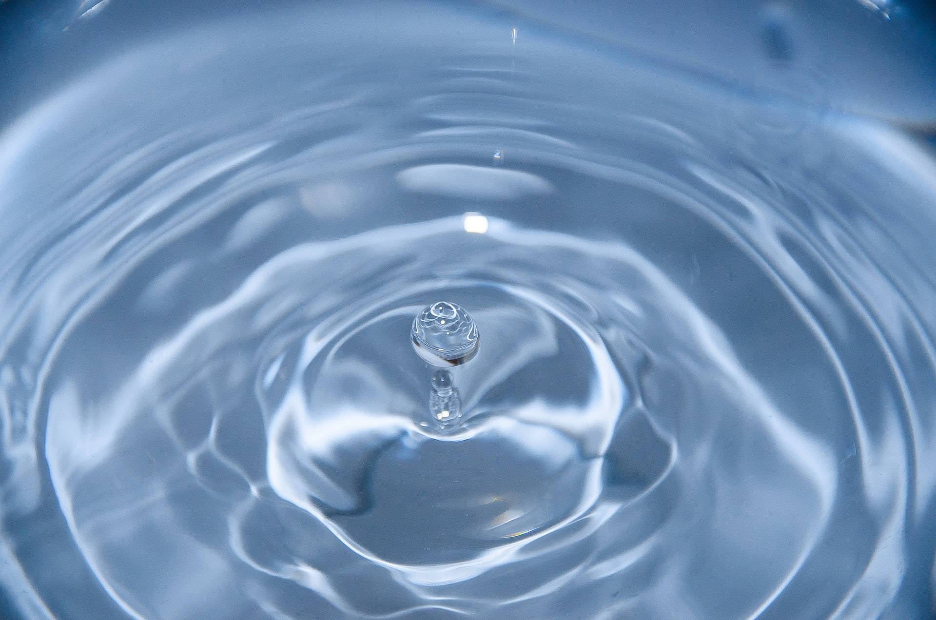 水 桌布 壁紙 — 一滴水珠懸浮在漣漪的藍色表面上，以超近距離細節形成同心圓。