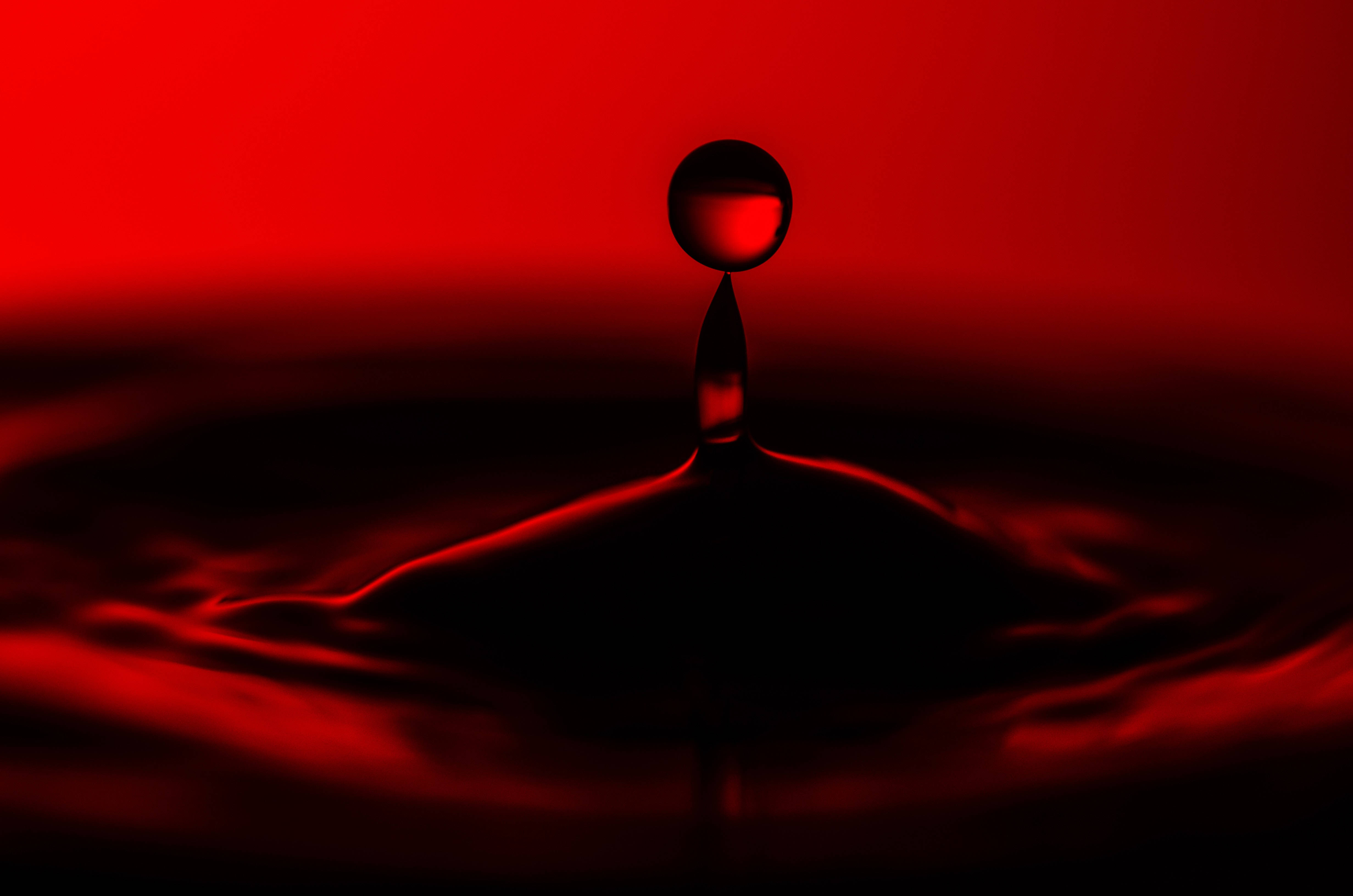 Cool Red And Black 桌布 壁紙 — 一滴紅色液滴懸浮在漣漪液體表面之上，背景為深紅漸變色。