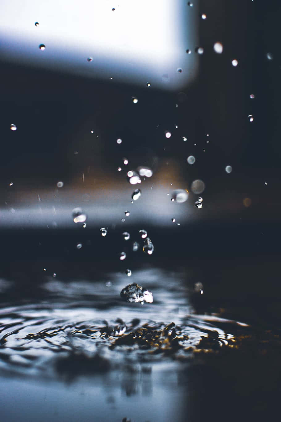 Water Drop 桌布 壁紙 — 一滴雨點濺入暗水中，在模糊的背景上產生漣漪和飛濺的水滴。