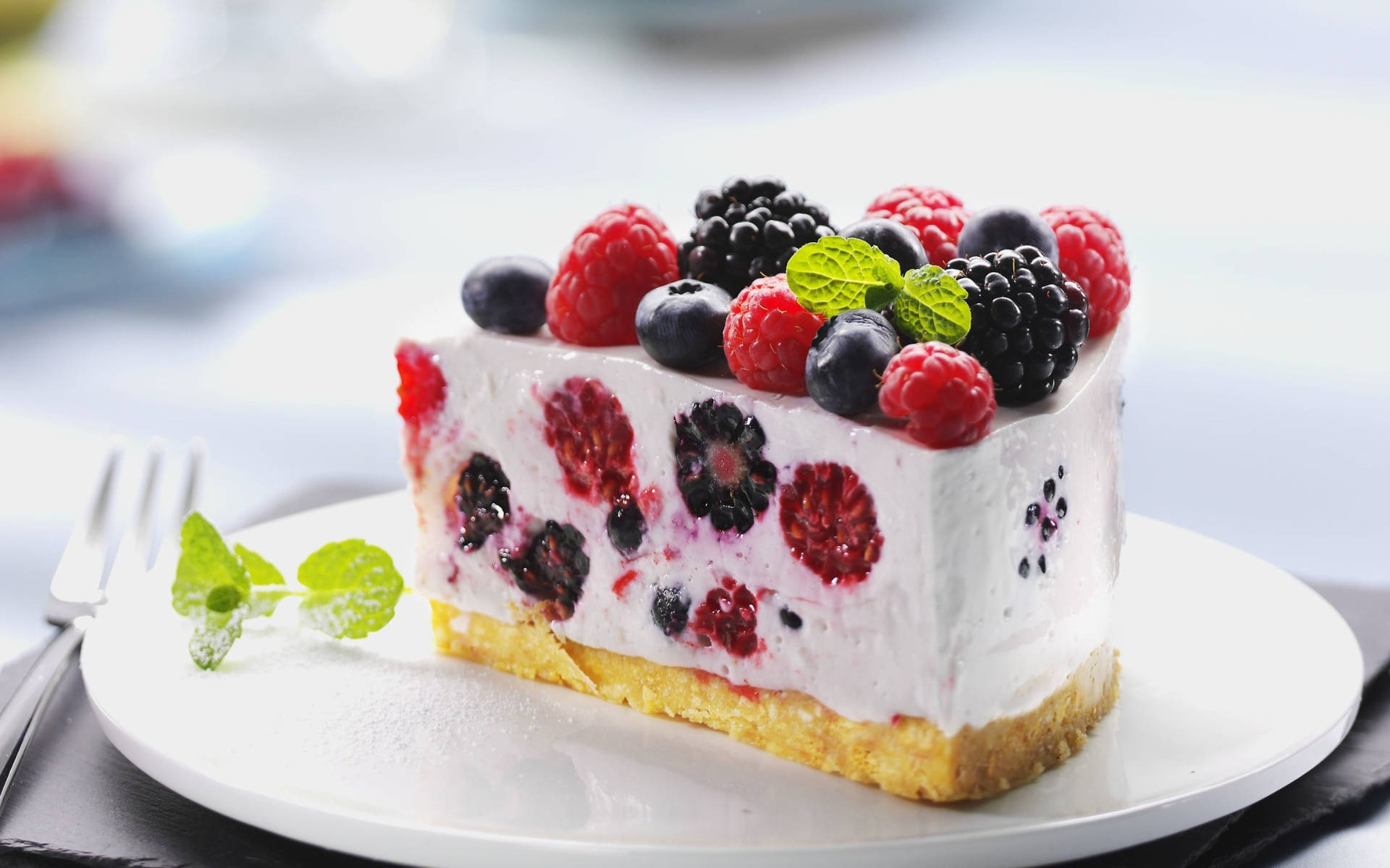 Berry 桌布 壁紙 — 一片 creamy 莓果起司蛋糕，上面鋪滿新鮮覆盆子、黑莓和藍莓，並以薄荷葉點綴，放在白色盤子上。