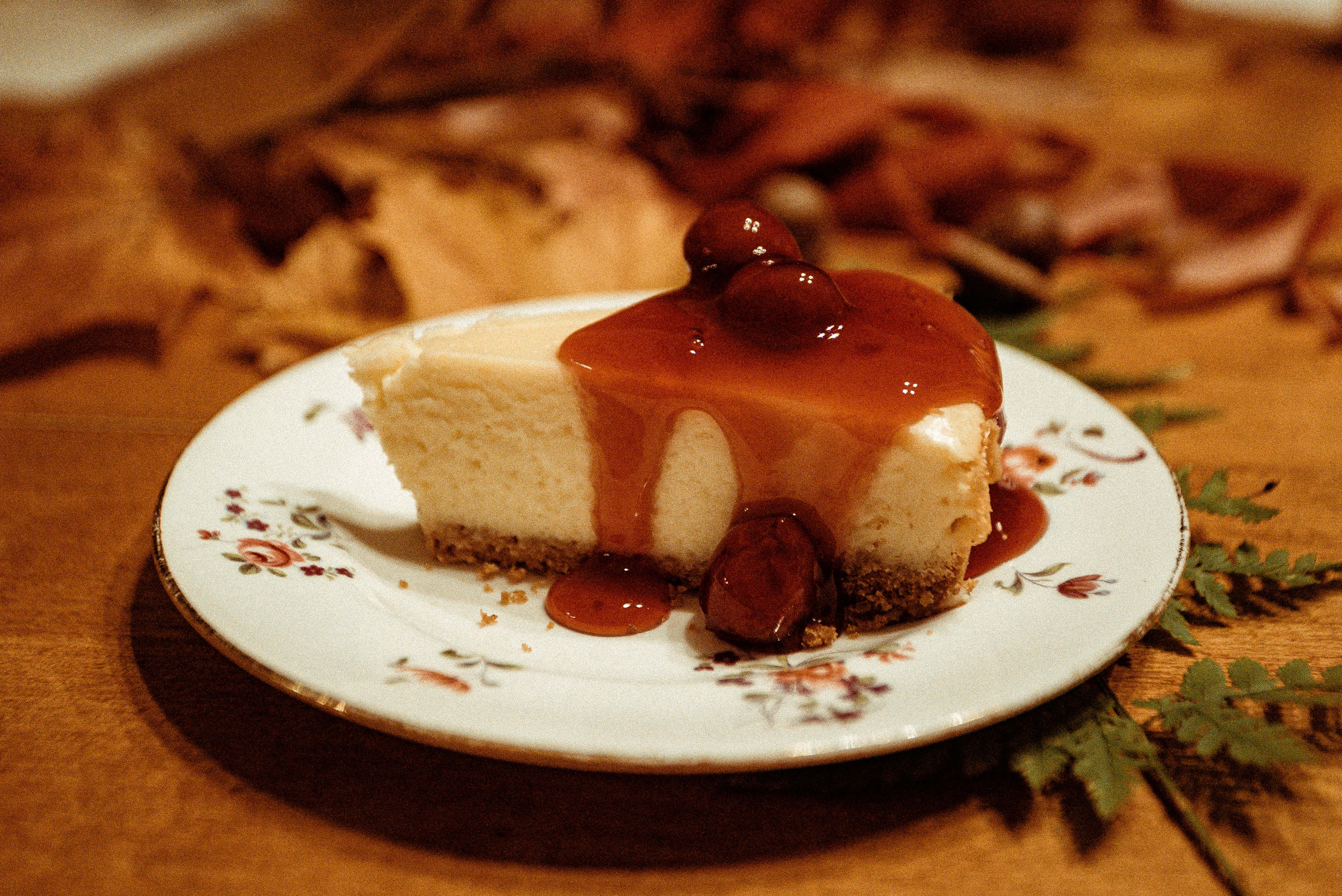 Caramel 桌布 壁紙 — 一片 creamy 起司蛋糕，上面鋪滿光澤的櫻桃醬和整顆櫻桃，放在花卉圖案的盤子上，襯以溫暖的木質背景。