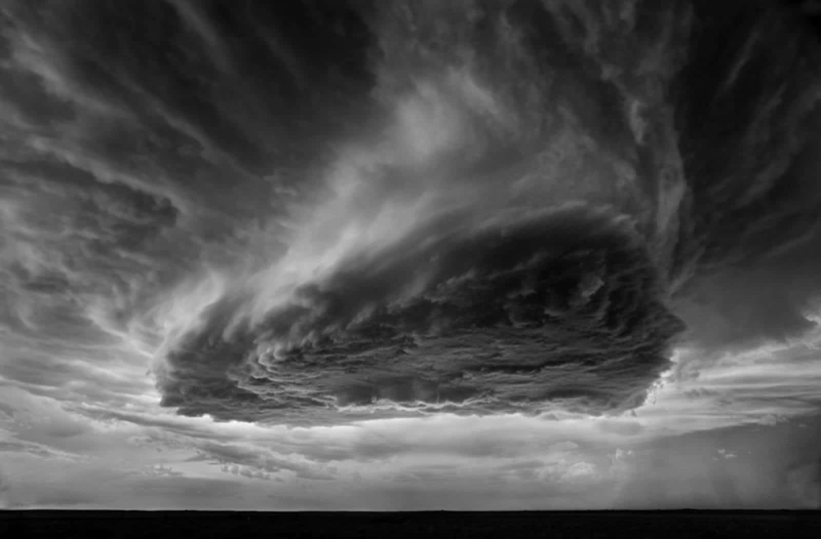 Black And White Storm 桌布 壁紙 — 一片充滿戲劇性的單色天空，旋轉的暴風雲籠罩在平坦的地平線上。