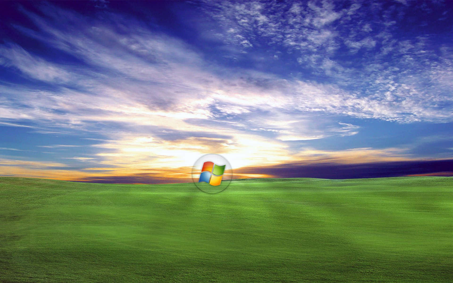 Windows XP 桌布 壁紙 — 一片充滿活力的綠色田野在戲劇性的日落天空下延伸，Windows 標誌漂浮在中央。