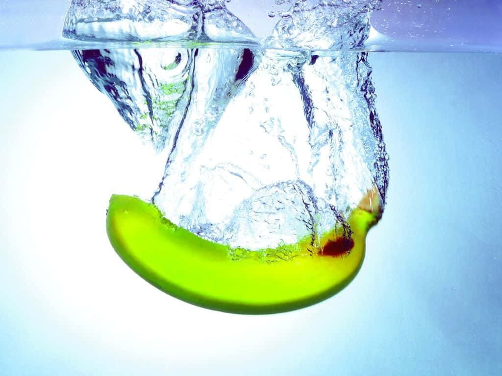 Fruit 桌布 壁紙 — 一片充滿活力的青蘋果片落入清澈的水中，在柔和的藍色漸變背景上產生動態的氣泡和漣漪。