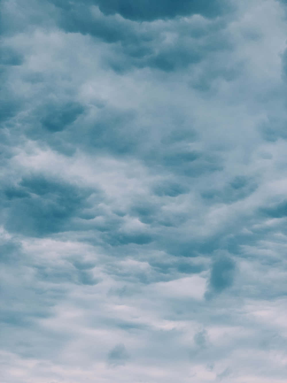 Weather 桌布 壁紙 — 一片充滿質感的青綠色和灰色雲朵，在柔和陰沉的地平線上飄移，營造出陰鬱的天空。