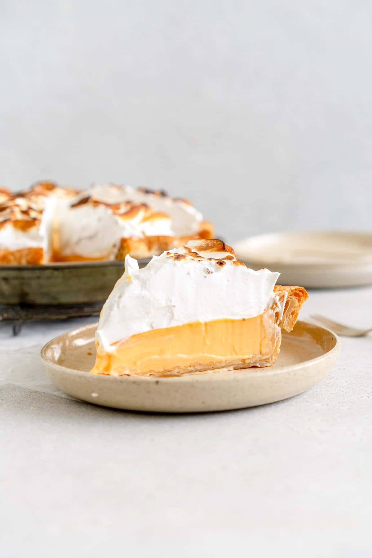 Meringue 桌布 壁紙 — 一片奶油檸檬蛋白派配烤蛋白，放在米色盤子上，背景中其餘的派模糊。
