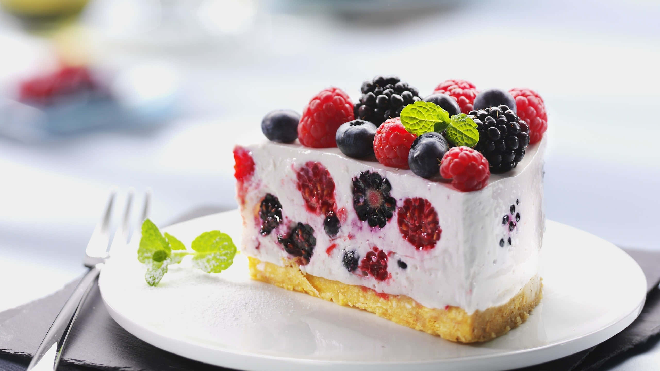 Spring Desserts 桌布 壁紙 — 一片奶油莓果起司蛋糕，上面鋪滿新鮮的覆盆子、黑莓和藍莓，並以薄荷葉點綴。