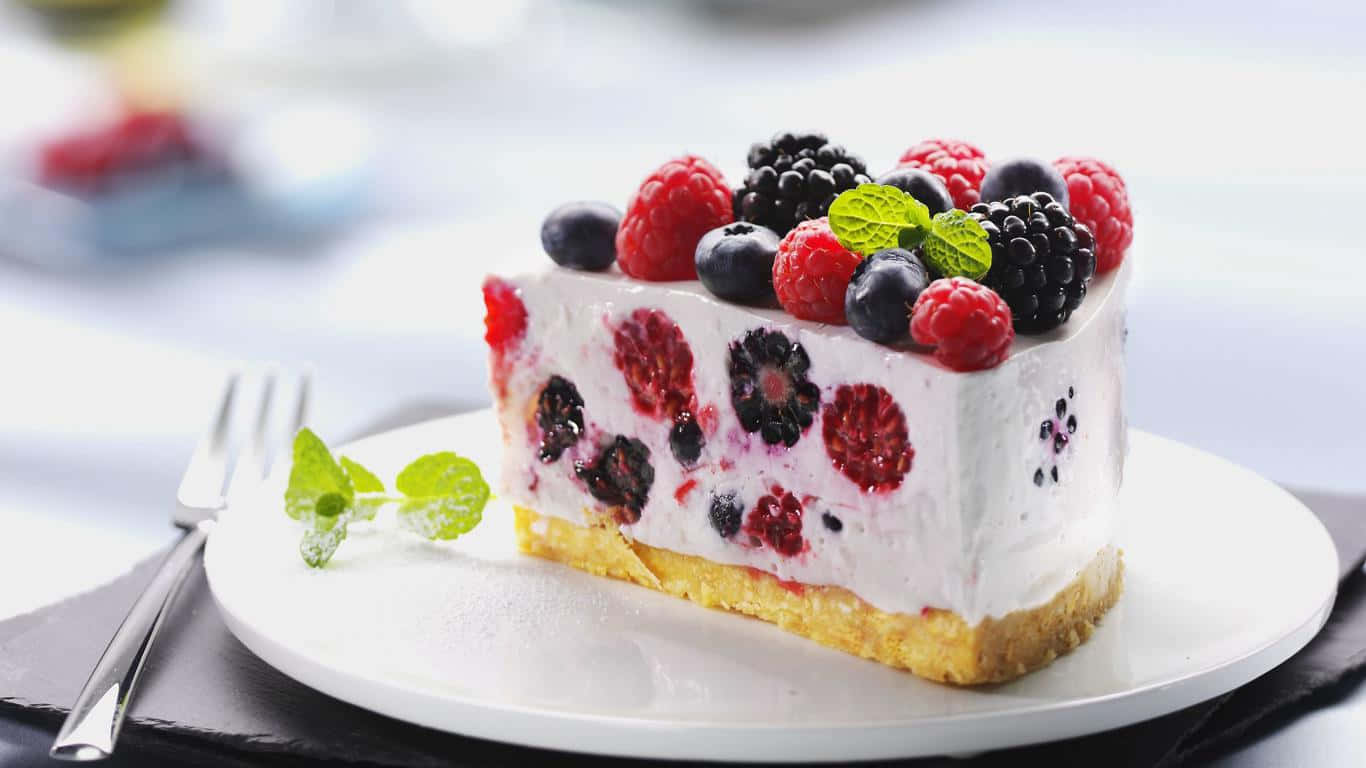 1366x768 Desserts 桌布 壁紙 — 一片奶油莓果起司蛋糕，上面鋪滿新鮮覆盆子、黑莓和藍莓，並以薄荷葉點綴，放在白色盤子上。
