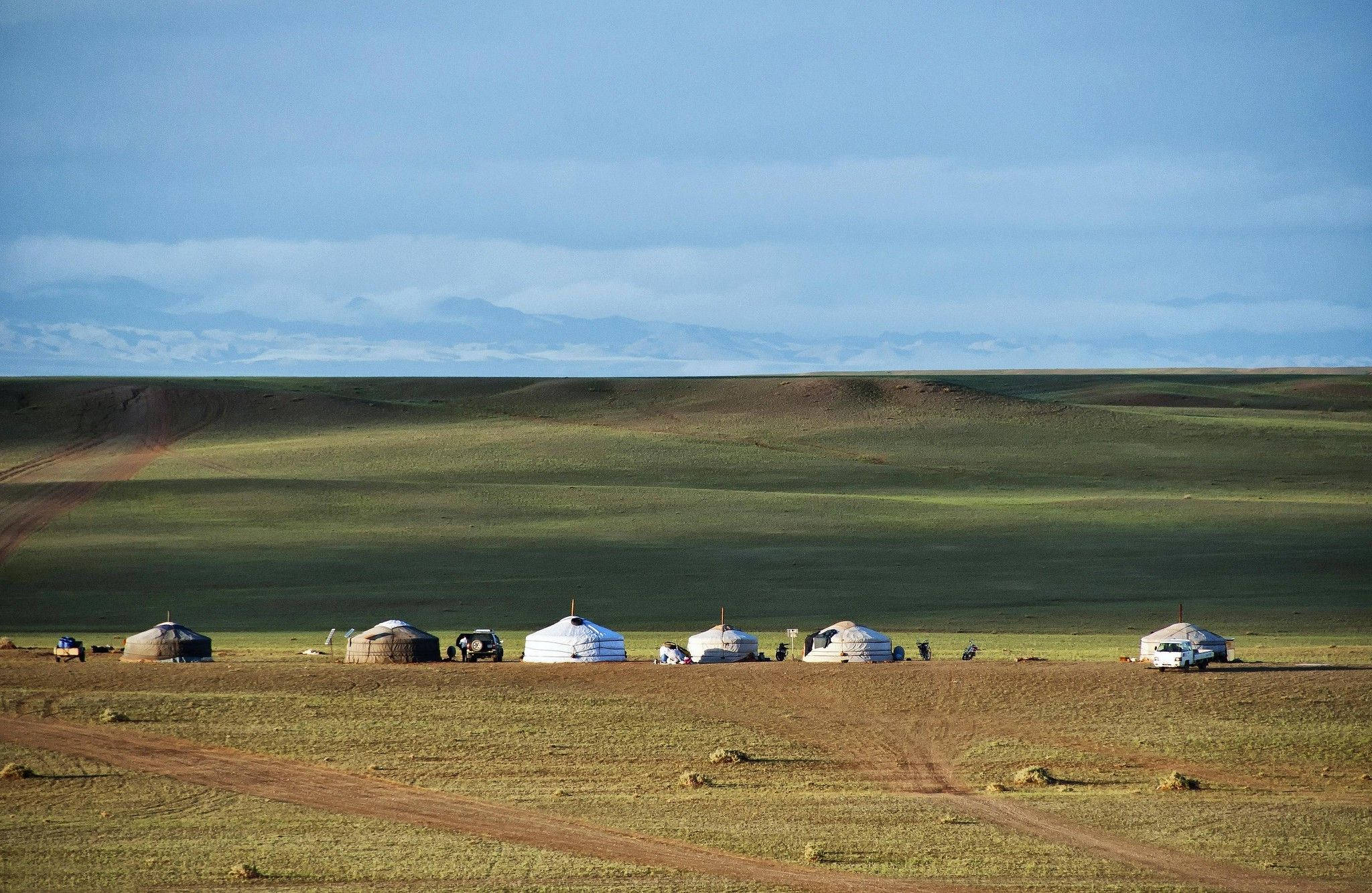 Mongolia 桌布 壁紙 — 一片寧靜的蒙古草原，散落著氈帳，廣闊的藍天下有遠方積雪的山峰。