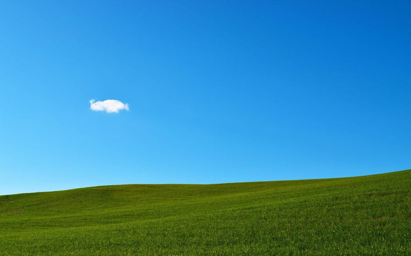 Windows 95 動態圖 桌布 壁紙 — 一片廣闊的綠色山丘在清澈的藍天下延伸，上方飄著一朵蓬鬆的白雲。