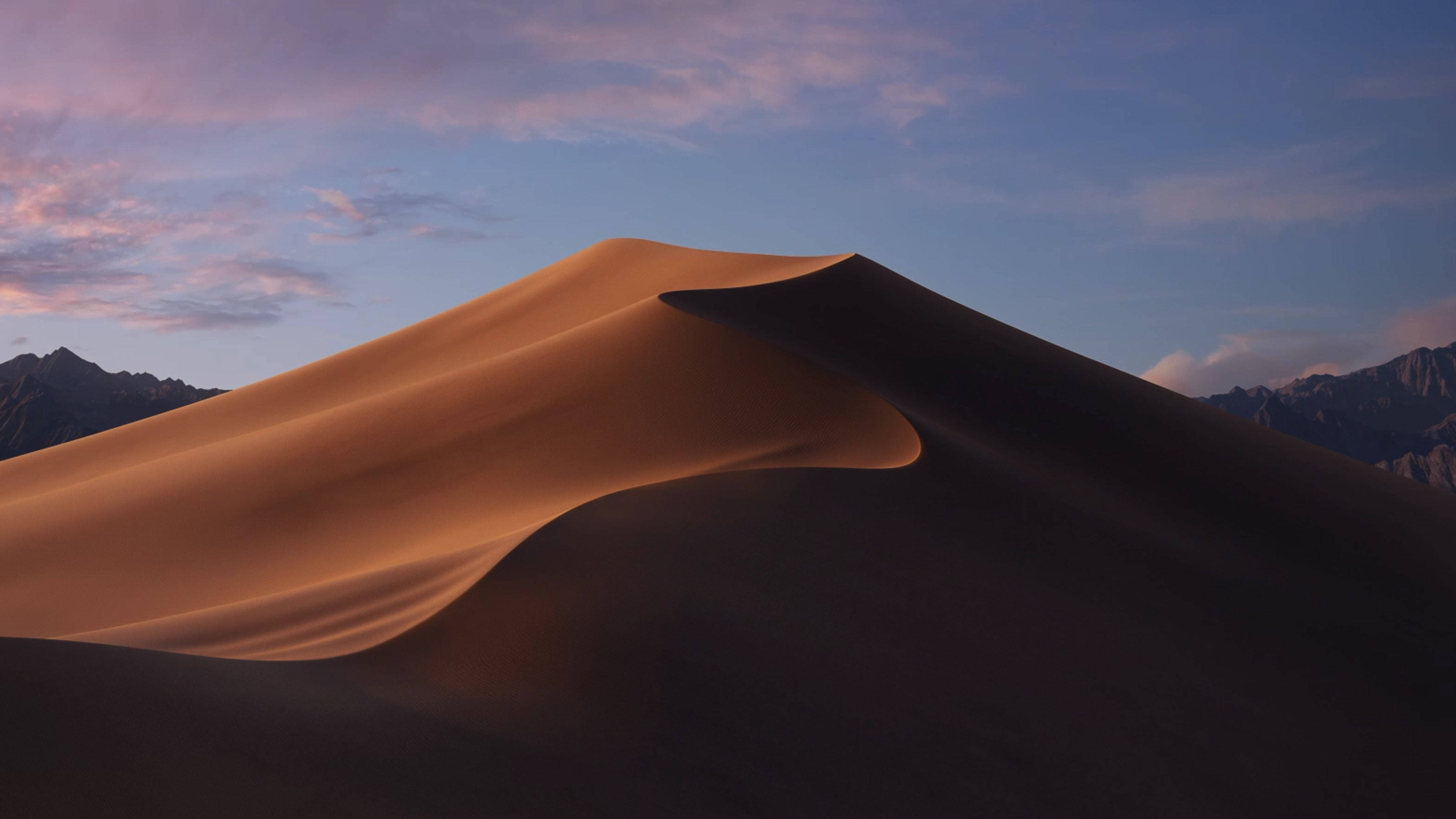Desert 桌布 壁紙 — 一片廣闊的金色沙丘在暮色天空下彎曲，天空中有柔和的粉紅色和藍色雲彩，遠山在陰影中。