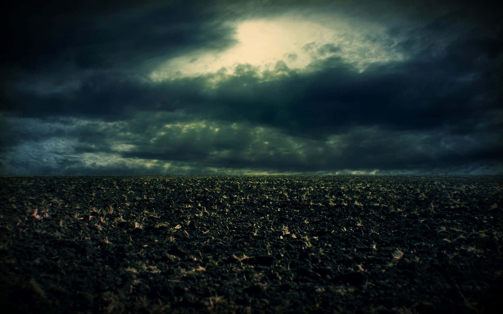 Dark Storm 桌布 壁紙 — 一片廣闊的黑暗田野在陰沉天空下延伸，一道光束穿透厚重的雲層。