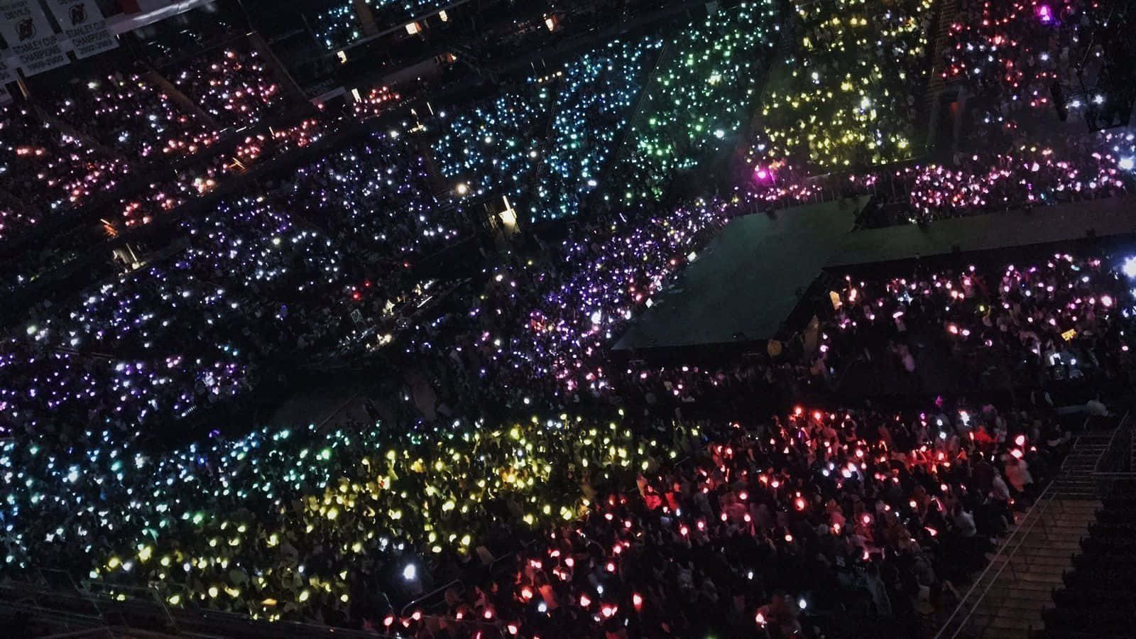 Bts Army Bomb 桌布 壁紙 — 一片彩虹色調的發光手機燈海充滿了黑暗的演唱會場地，在人群上方創造出耀眼的星海。