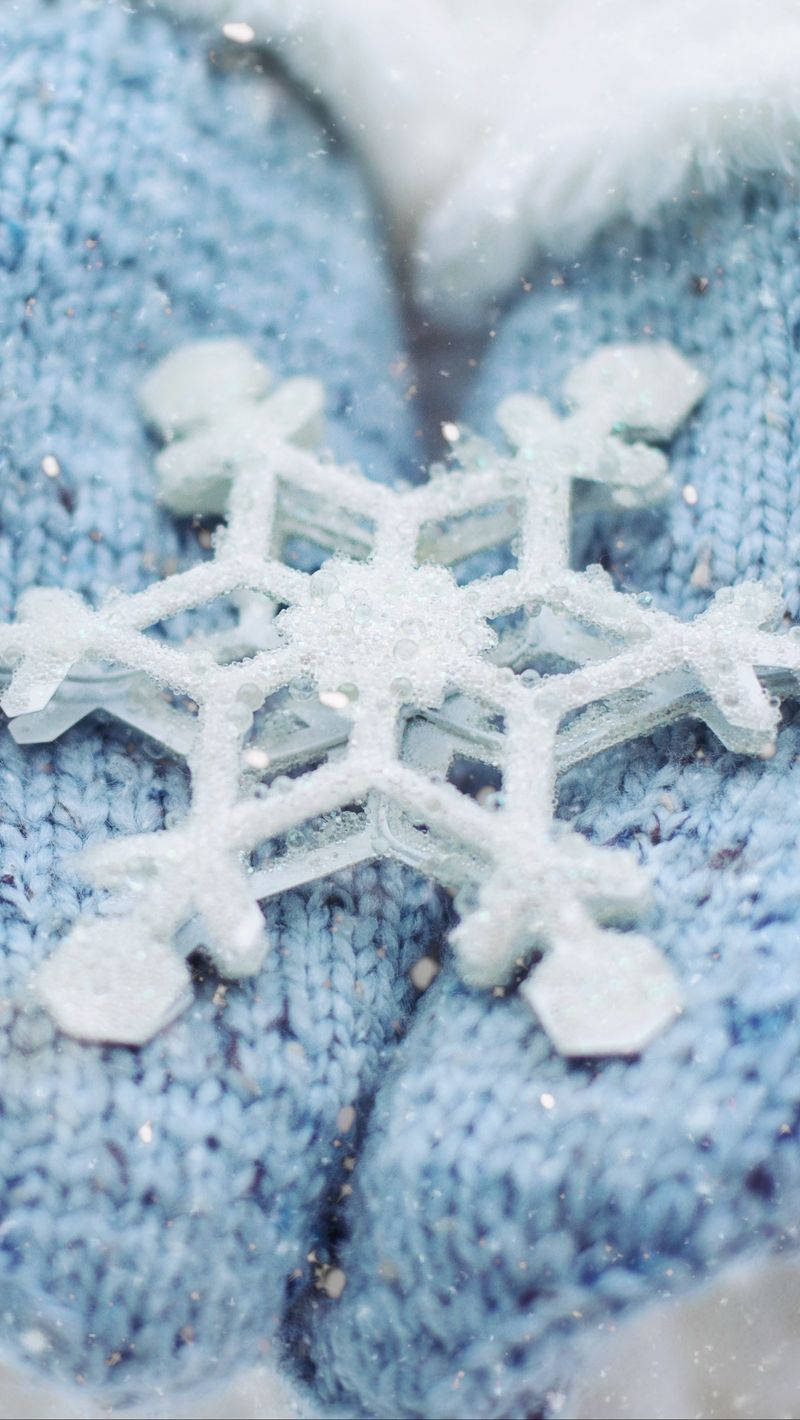 聖誕節 桌布 壁紙 — 一片精緻的雪花在冬日特寫中，輕輕落在柔軟的藍色針織手套上。