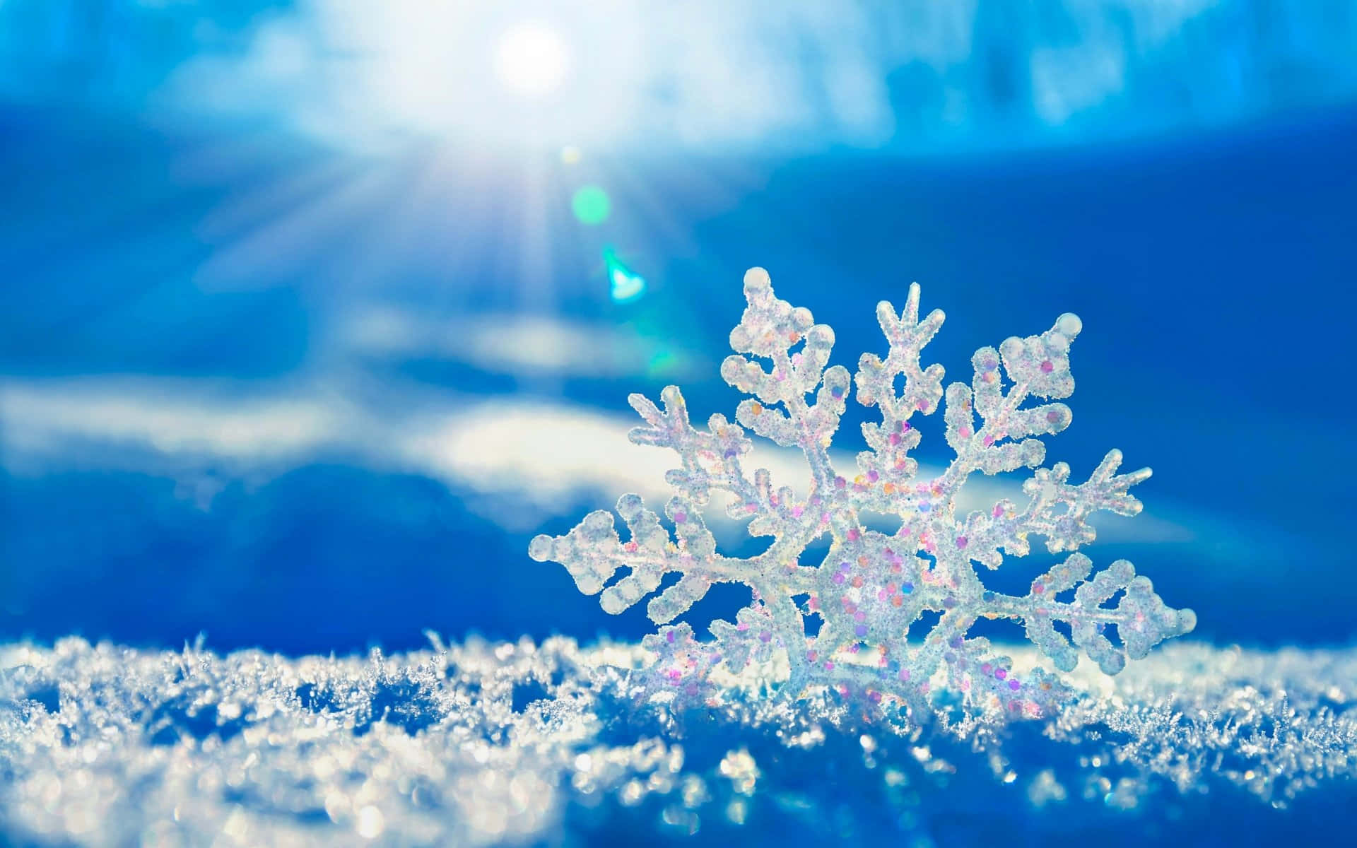 Beautiful Winter 桌布 壁紙 — 一片精緻的雪花在銳利焦點中閃閃發光，背景是充滿活力的藍色雪景，陽光穿透其中。