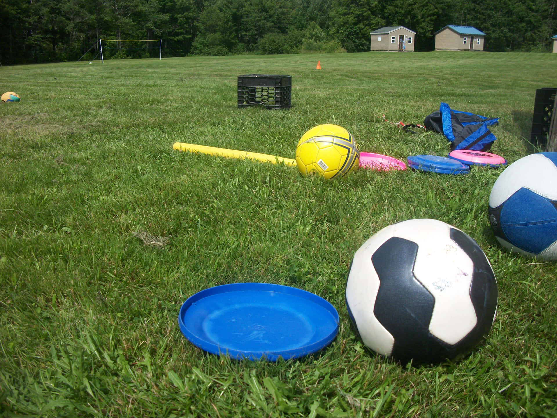 Outdoor Activities 桌布 壁紙 — 一片草地上散落著色彩繽紛的運動裝備，包括足球、飛盤和一支黃色球棒，在明亮的日光下。