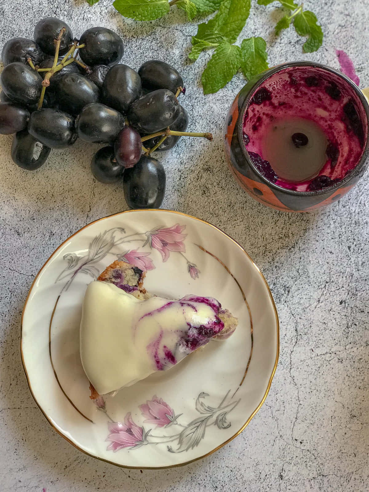 Fruit 桌布 壁紙 — 一片莓果起司蛋糕放在花卉圖案盤子上，旁邊有黑葡萄和紫色飲料，置於有紋理的表面上。