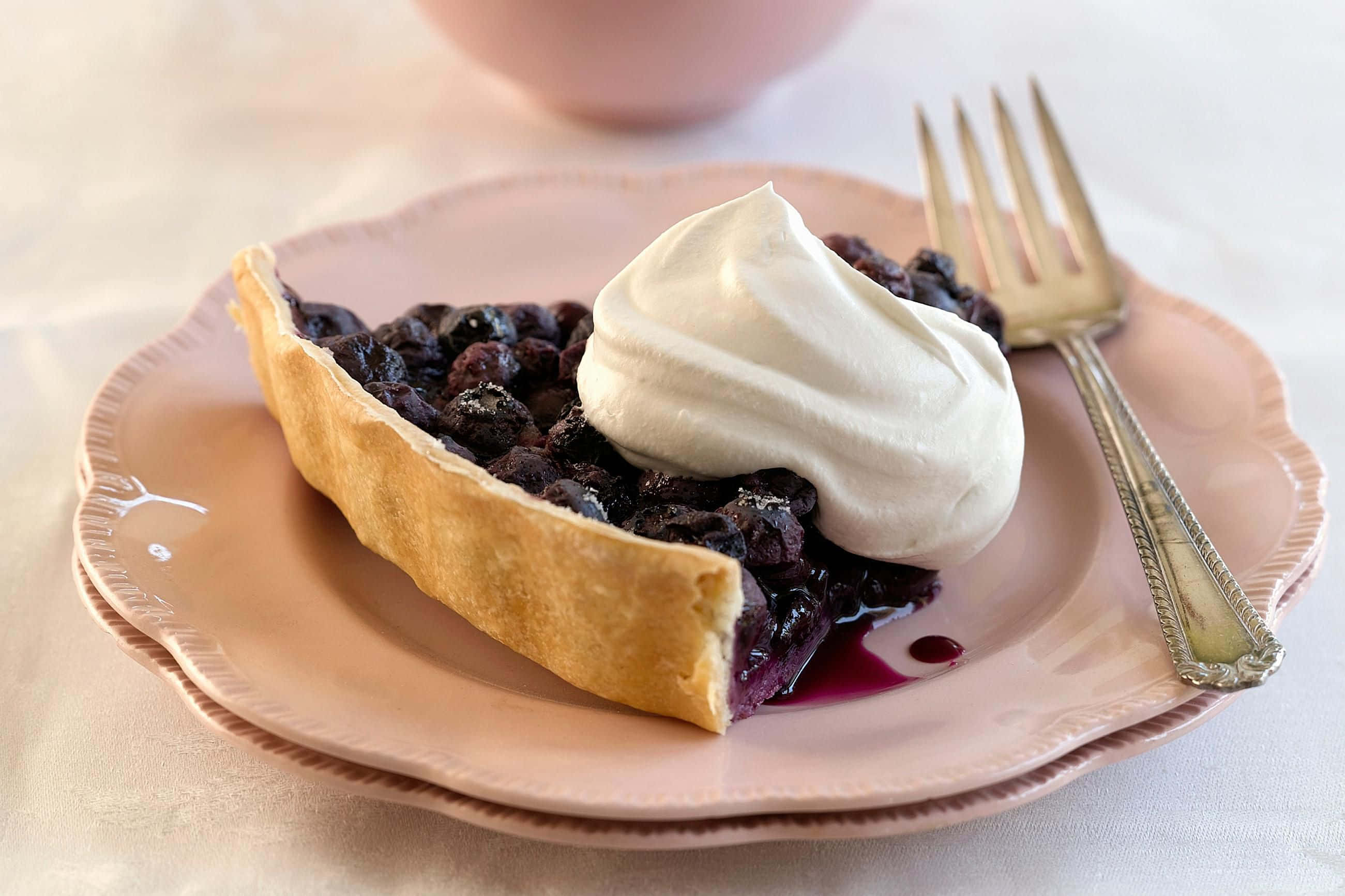 Blueberry Pie 桌布 壁紙 — 一片藍莓派搭配鮮奶油放在粉紅色盤子上，旁邊有一把復古叉子。