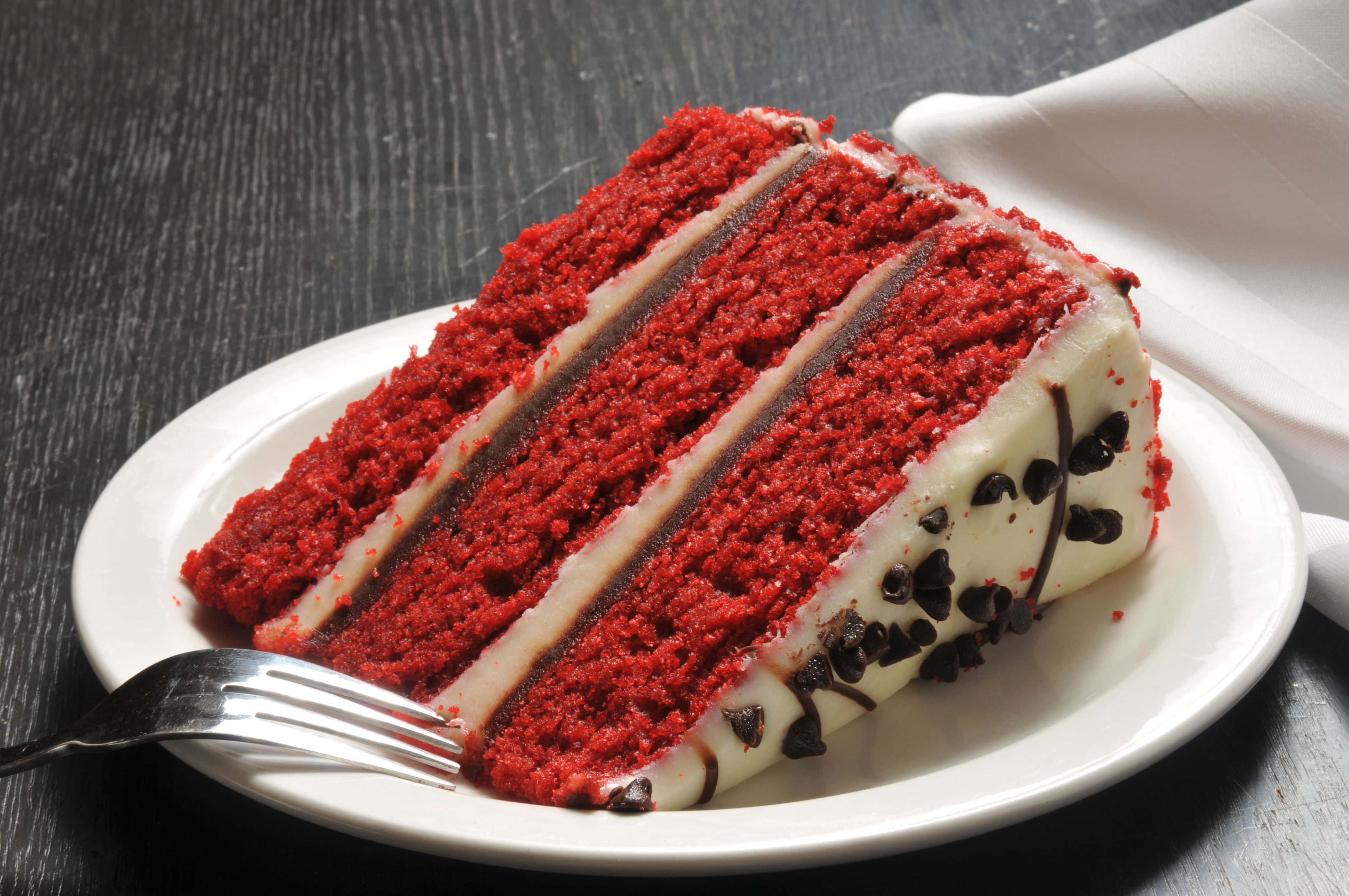 Red Velvet Cake 桌布 壁紙 — 一片豐富的紅絲絨蛋糕，配上奶油乳酪糖霜和巧克力淋醬，放在白色盤子上，旁邊有一把叉子。