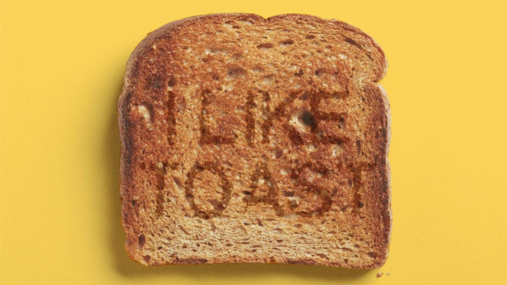 Bread 桌布 壁紙 — 一片金黃色的吐司，表面烤有「I LIKE TOAST」字樣，背景為鮮黃色。