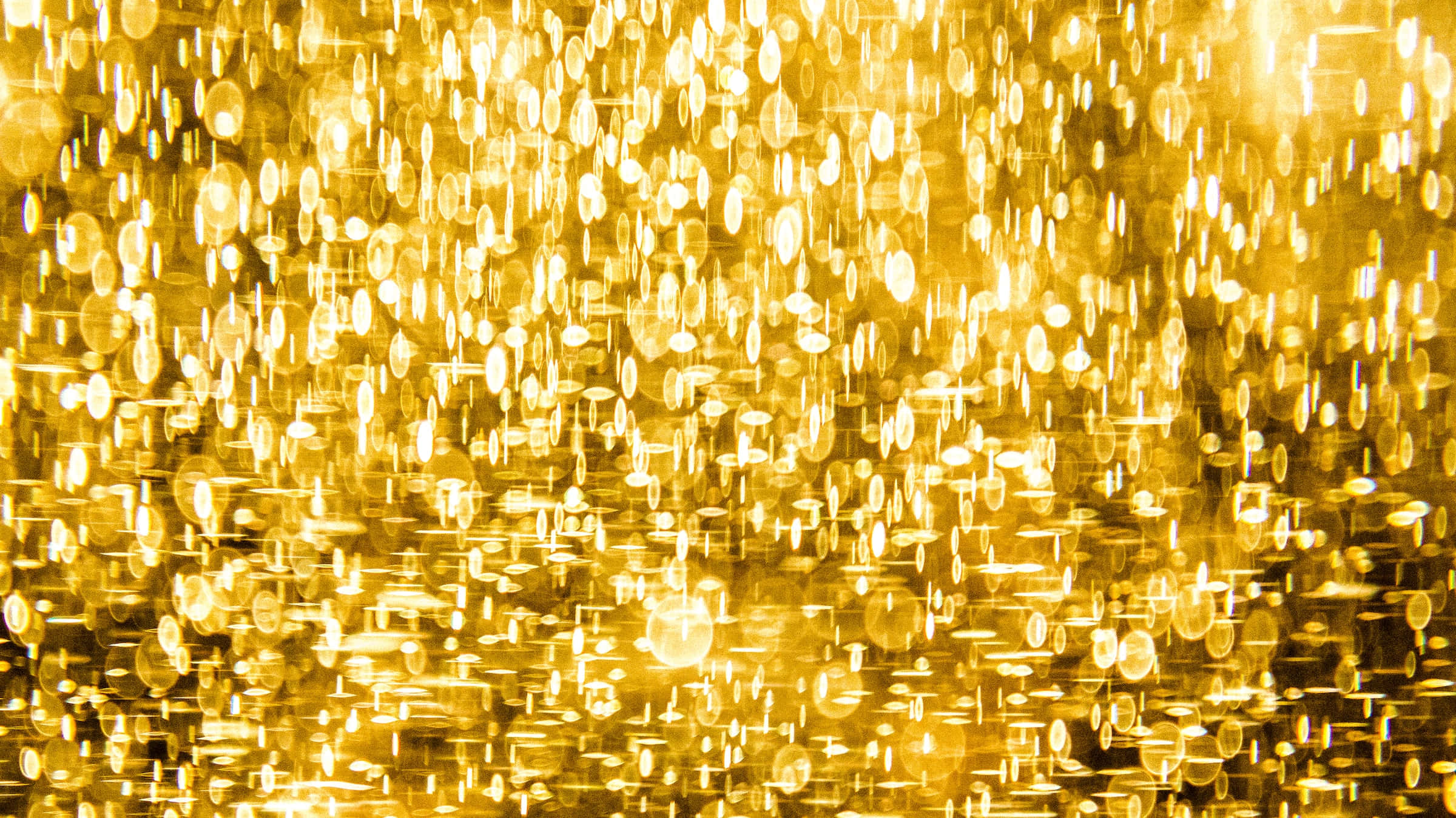 Golden Light 桌布 壁紙 — 一片閃爍的金色散景圓圈，在黑暗背景下散發溫暖光芒。