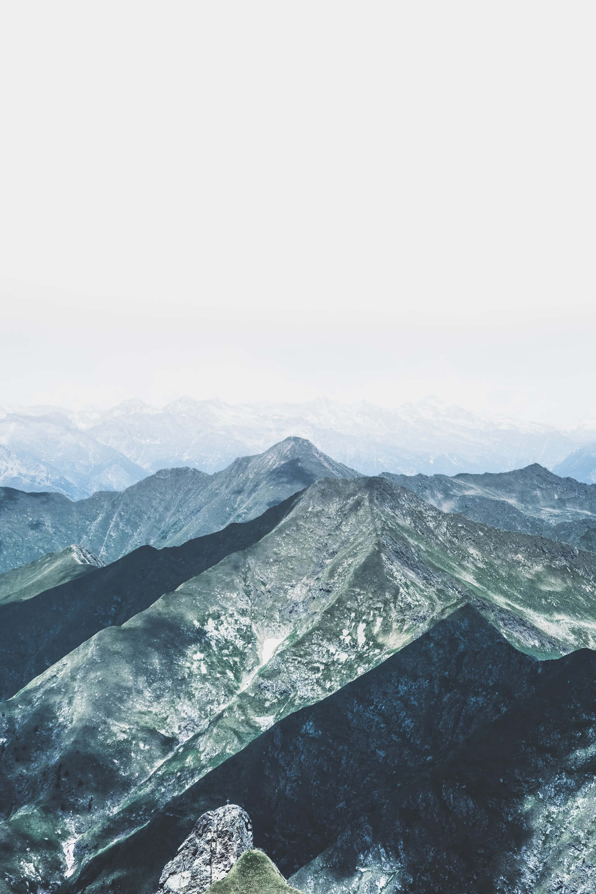山景 桌布 壁紙 — 一片霧氣瀰漫的山脈延伸至遠方，層巒疊嶂，天空蒼白。