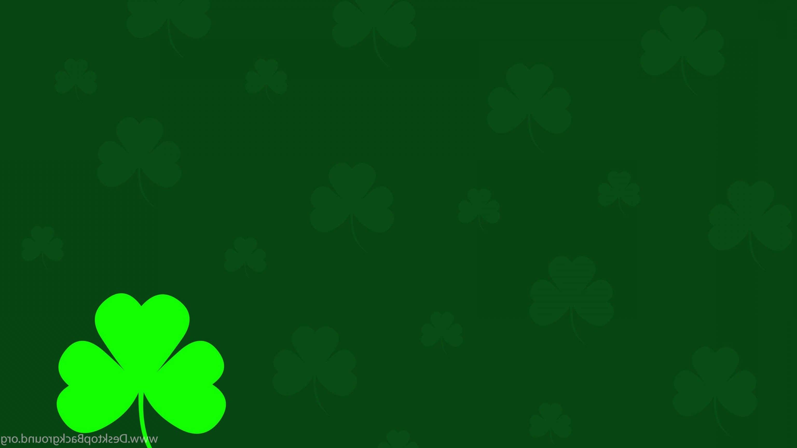 Shamrock 桌布 壁紙 — 一片鮮綠色的四葉草在帶有模糊三葉草圖案的深綠色背景上格外突出。