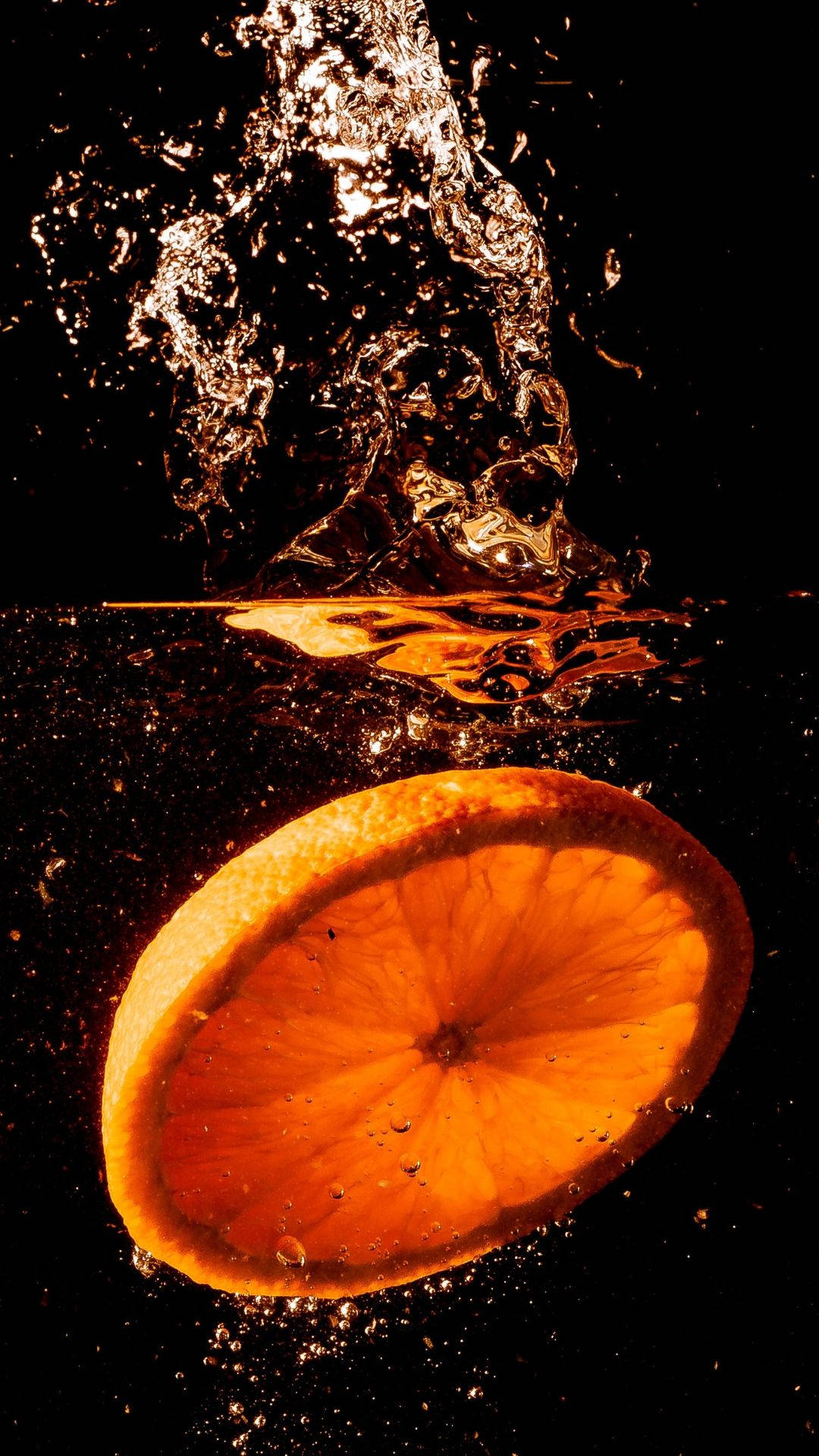 Orange Fruit 桌布 壁紙 — 一片鮮豔的橙片掉入水中，在黑色背景上形成戲劇性的水花。