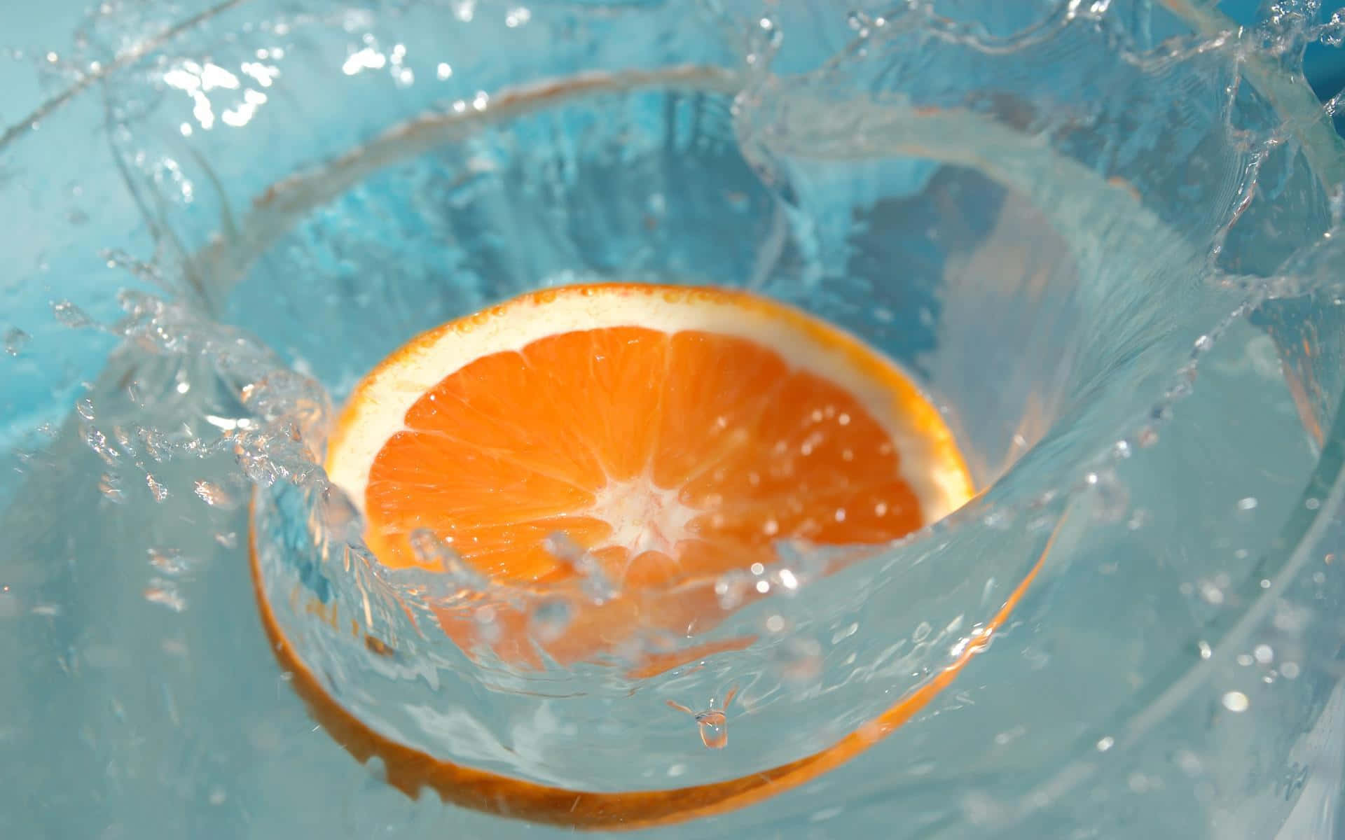 Refreshing 桌布 壁紙 — 一片鮮豔的橙片掉入清澈的藍色水中，產生動態的水花和漣漪。