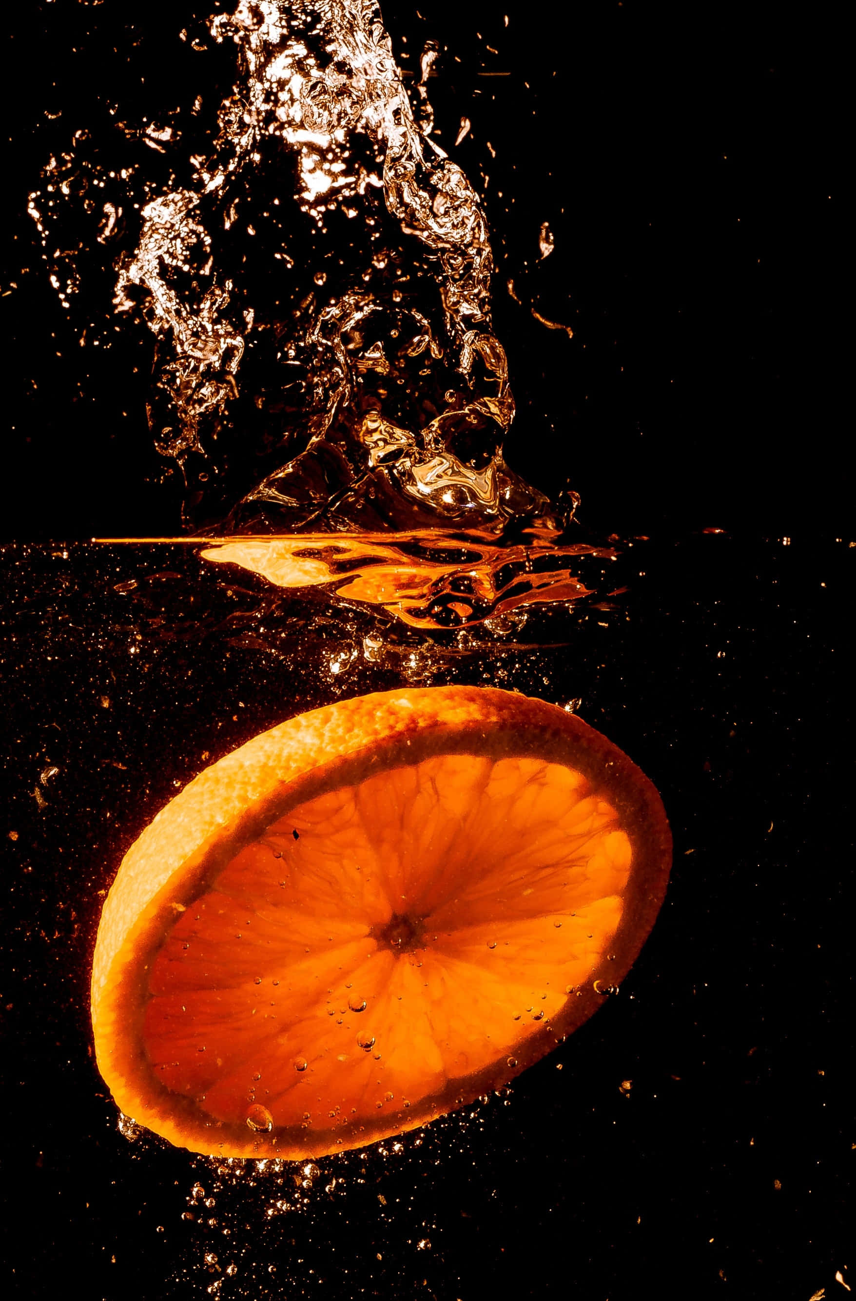 Orange Fruit 桌布 壁紙 — 一片鮮豔的橙片落入水中，在黑色背景上形成戲劇性的水花。
