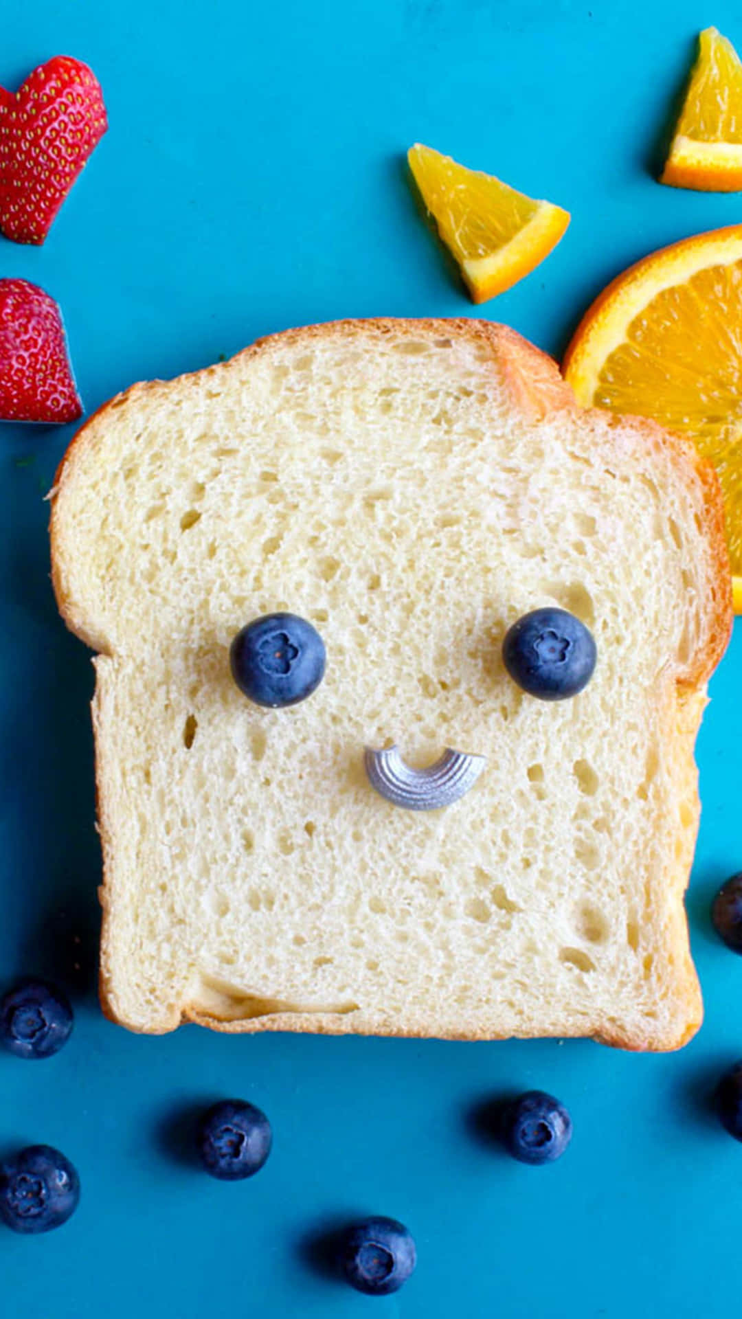 Cute Food iPhone 桌布 壁紙 — 一片麵包，用藍莓做眼睛，銀色牙籤做嘴巴，在明亮的藍色背景上，在草莓和柳橙片之間微笑。
