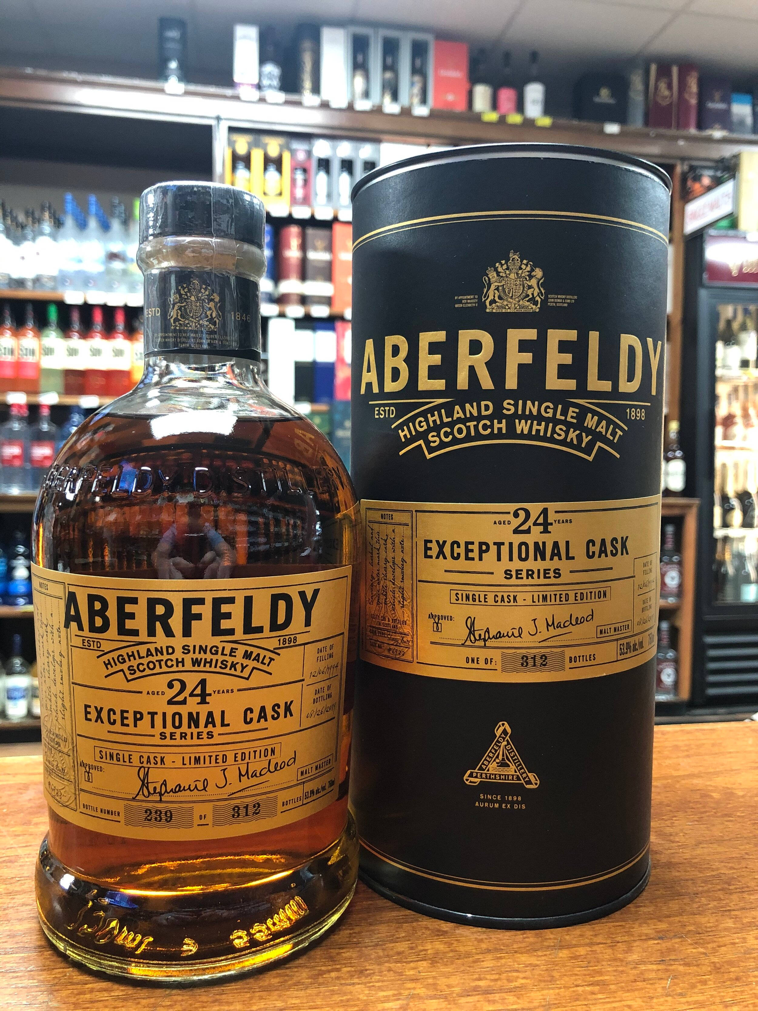 Drink 桌布 壁紙 — 一瓶 Aberfeldy 24 年 Exceptional Cask Series 威士忌連同包裝管放在木製吧檯上，後面有酒類貨架。