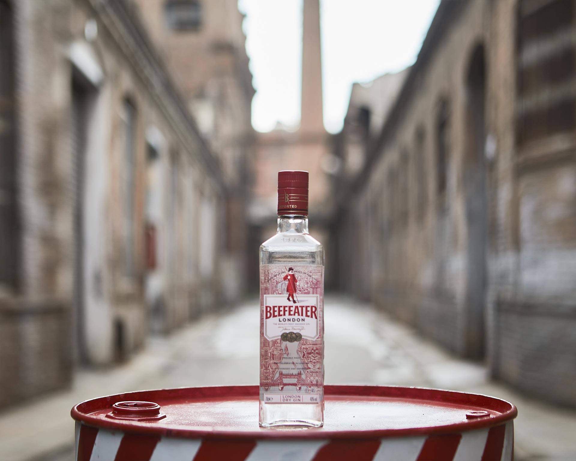 bottle 桌布 壁紙 — 一瓶 Beefeater London Gin 酒瓶放在狹窄磚砌小巷中一個紅白條紋桶的正中央。