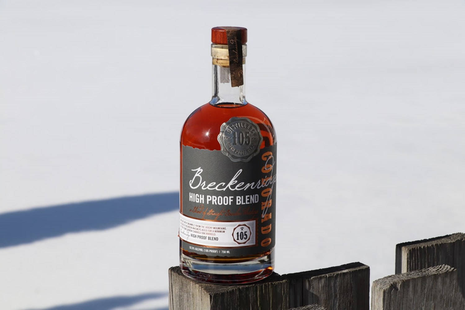 Drink 桌布 壁紙 — 一瓶 Breckenridge High Proof Blend 威士忌放在風化的木籬笆柱上，背景是明亮的陽光下的雪景。