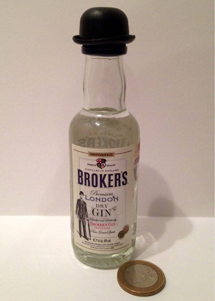 small 桌布 壁紙 — 一瓶 Brokers Premium London Dry Gin 迷你酒瓶，頂著黑色圓頂禮帽，放在白色平面上，旁邊有一枚歐元硬幣。