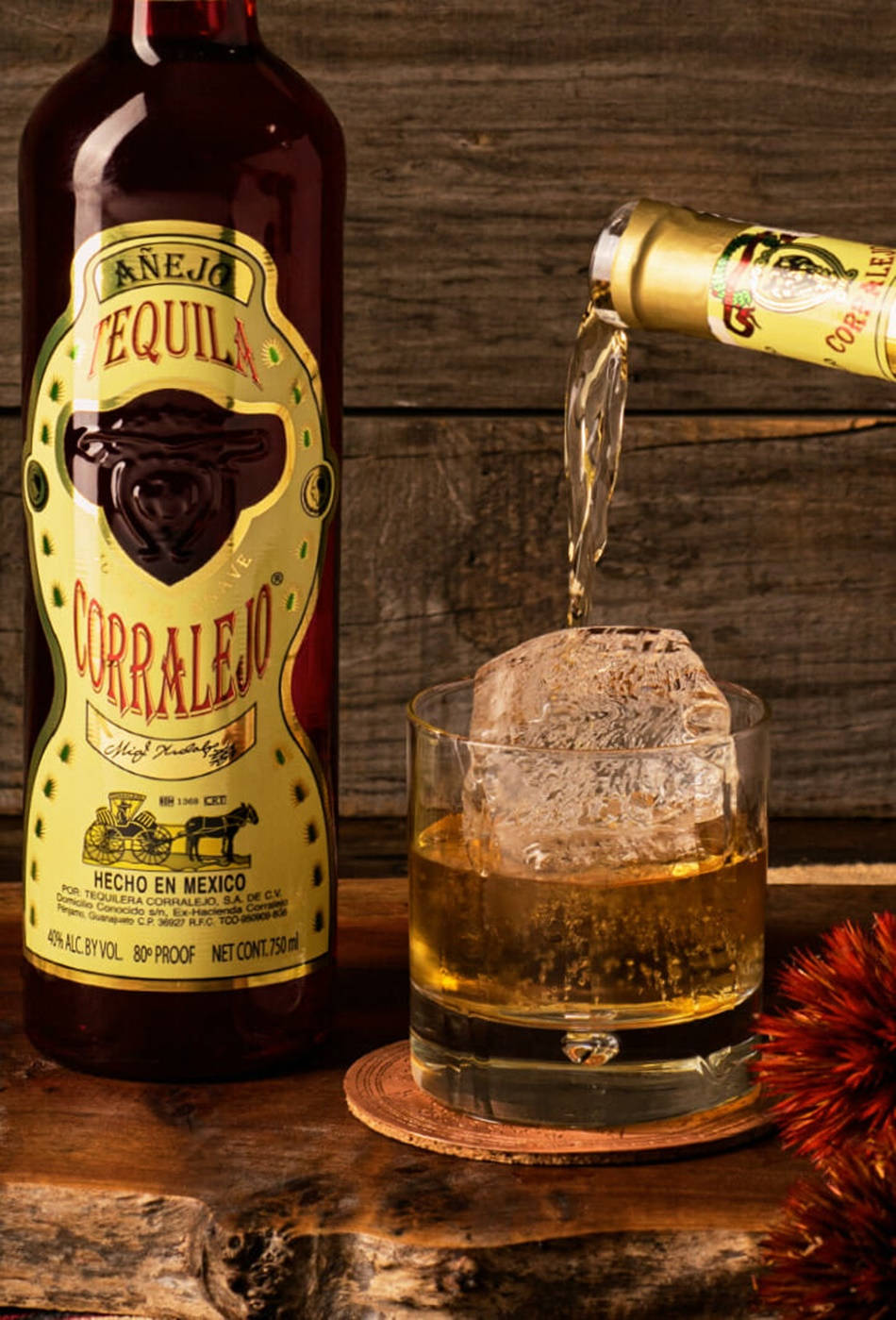 cocktail 桌布 壁紙 — 一瓶 Corralejo Añejo 龍舌蘭酒將金色液體倒在一個大冰塊上，倒入放在質樸木桌上的 rocks 杯中。
