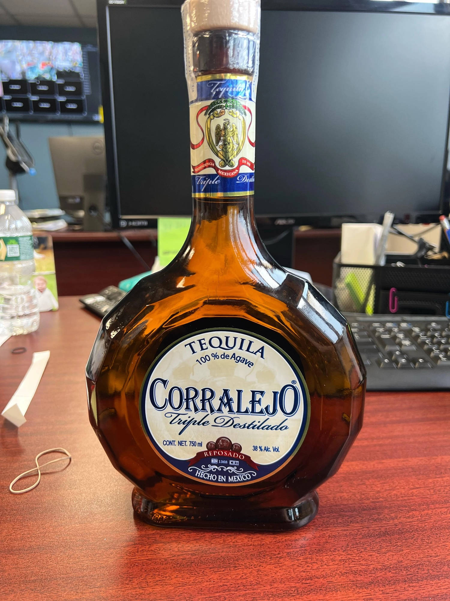 Drink 桌布 壁紙 — 一瓶 Corralejo Reposado 龍舌蘭酒放在辦公室木桌中央，背景有電腦顯示器和鍵盤。