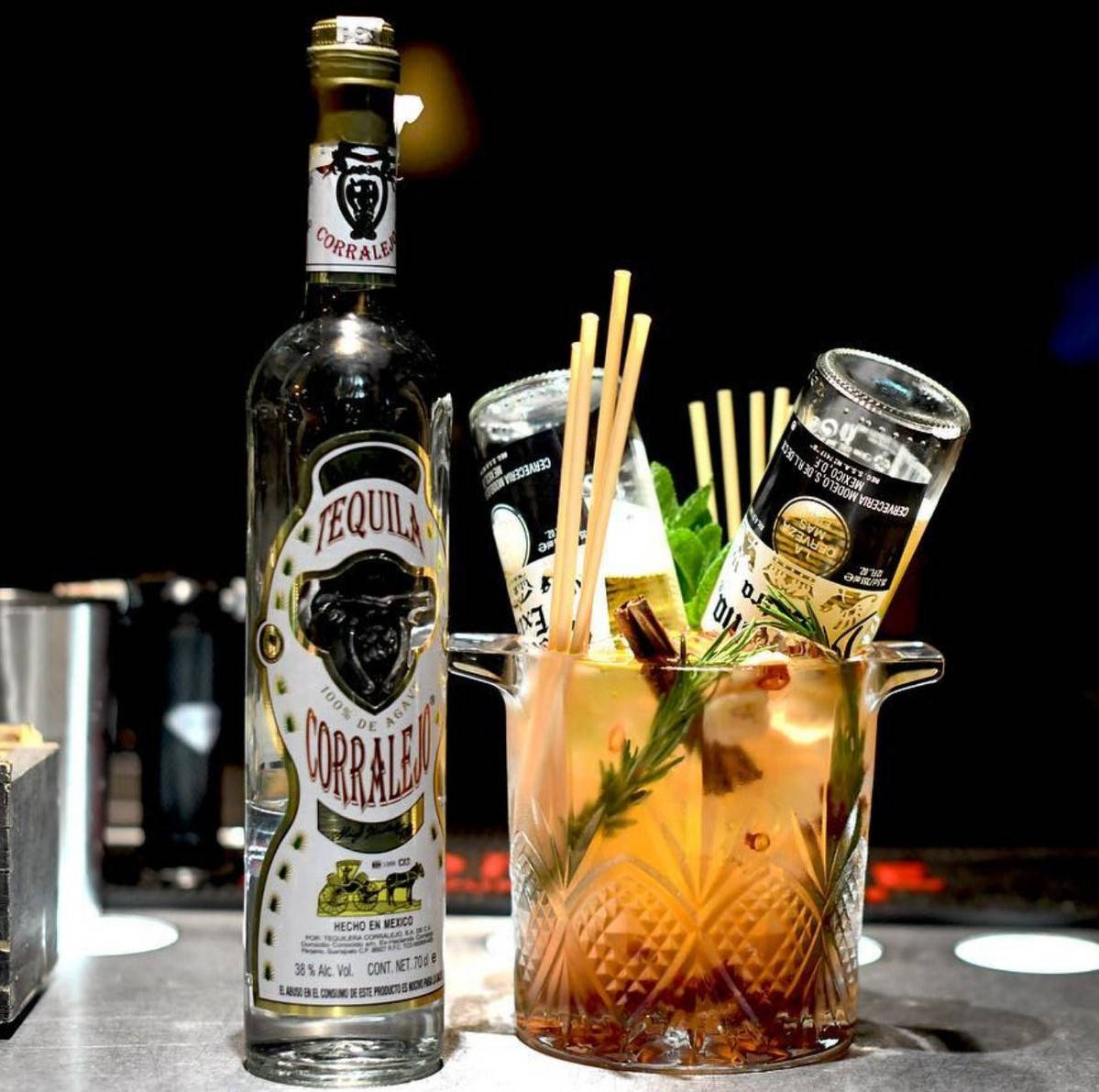 cocktail 桌布 壁紙 — 一瓶 Corralejo 龍舌蘭酒放在一個裝滿琥珀色雞尾酒的水晶杯旁邊，飾以迷迭香和肉桂棒。