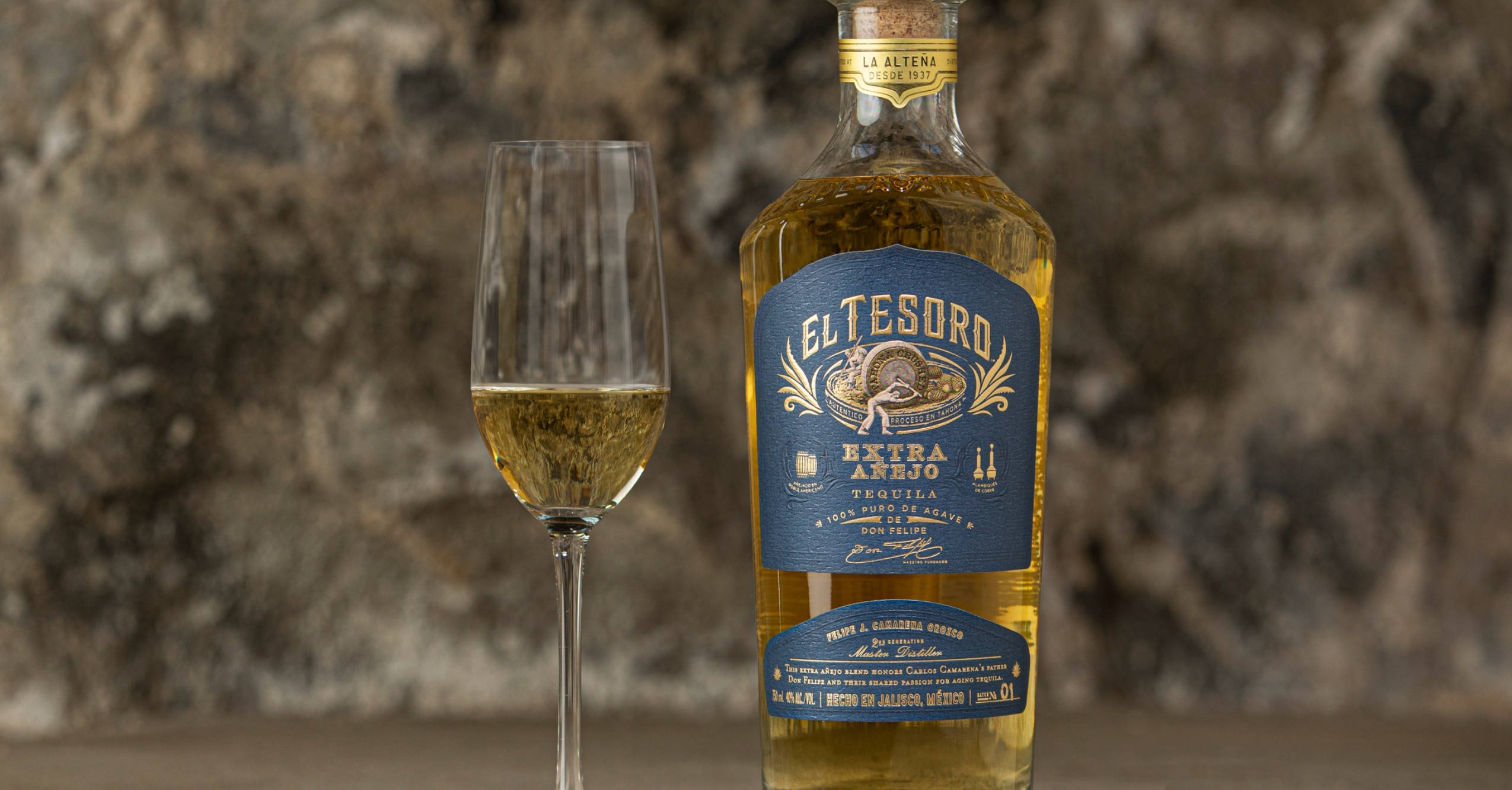 alcohol 桌布 壁紙 — 一瓶 El Tesoro Extra Añejo 龍舌蘭酒放在一個裝滿酒的笛形杯旁邊，背景是紋理石牆。