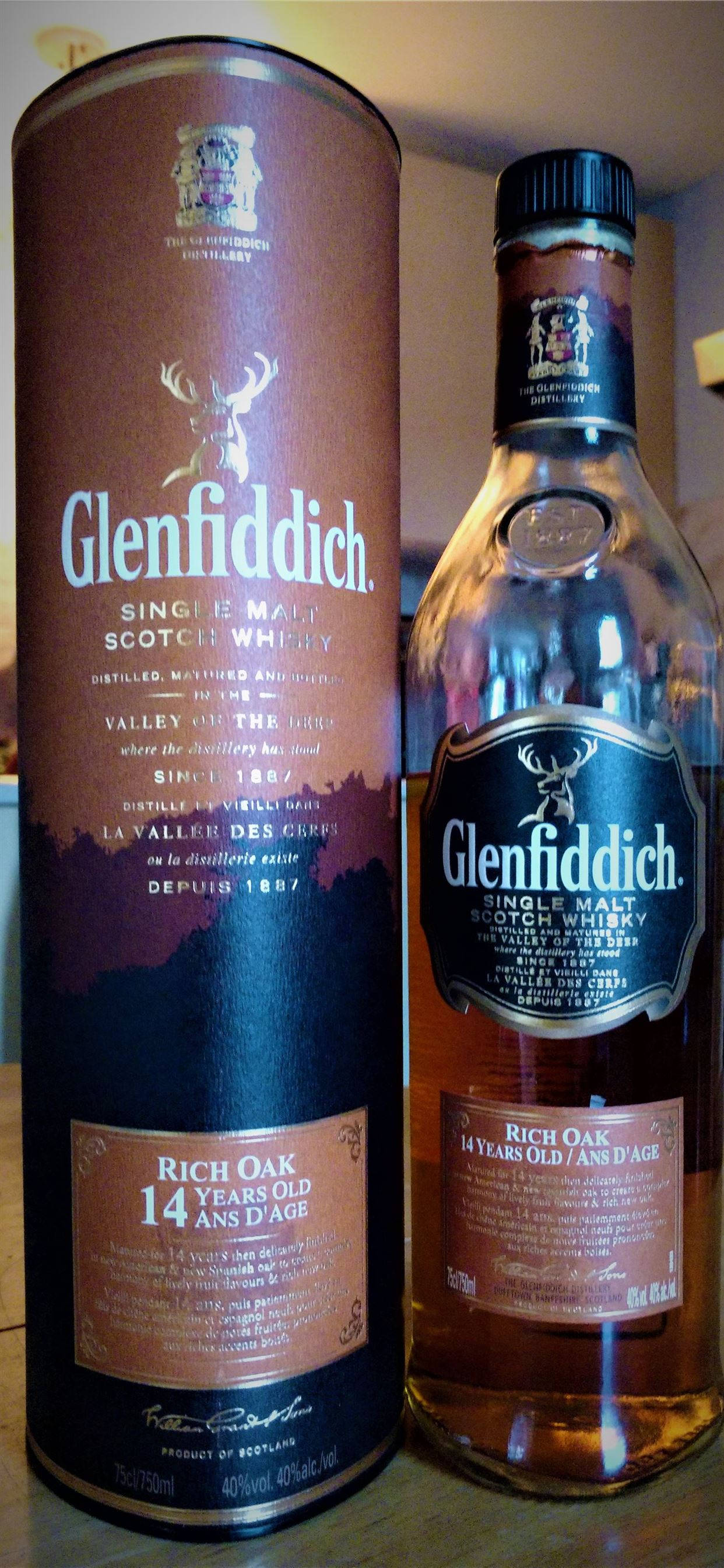 alcohol 桌布 壁紙 — 一瓶 Glenfiddich 14 年 Rich Oak 單一麥芽蘇格蘭威士忌，旁邊是其圓柱形棕色和金色盒子，帶有鹿標誌。