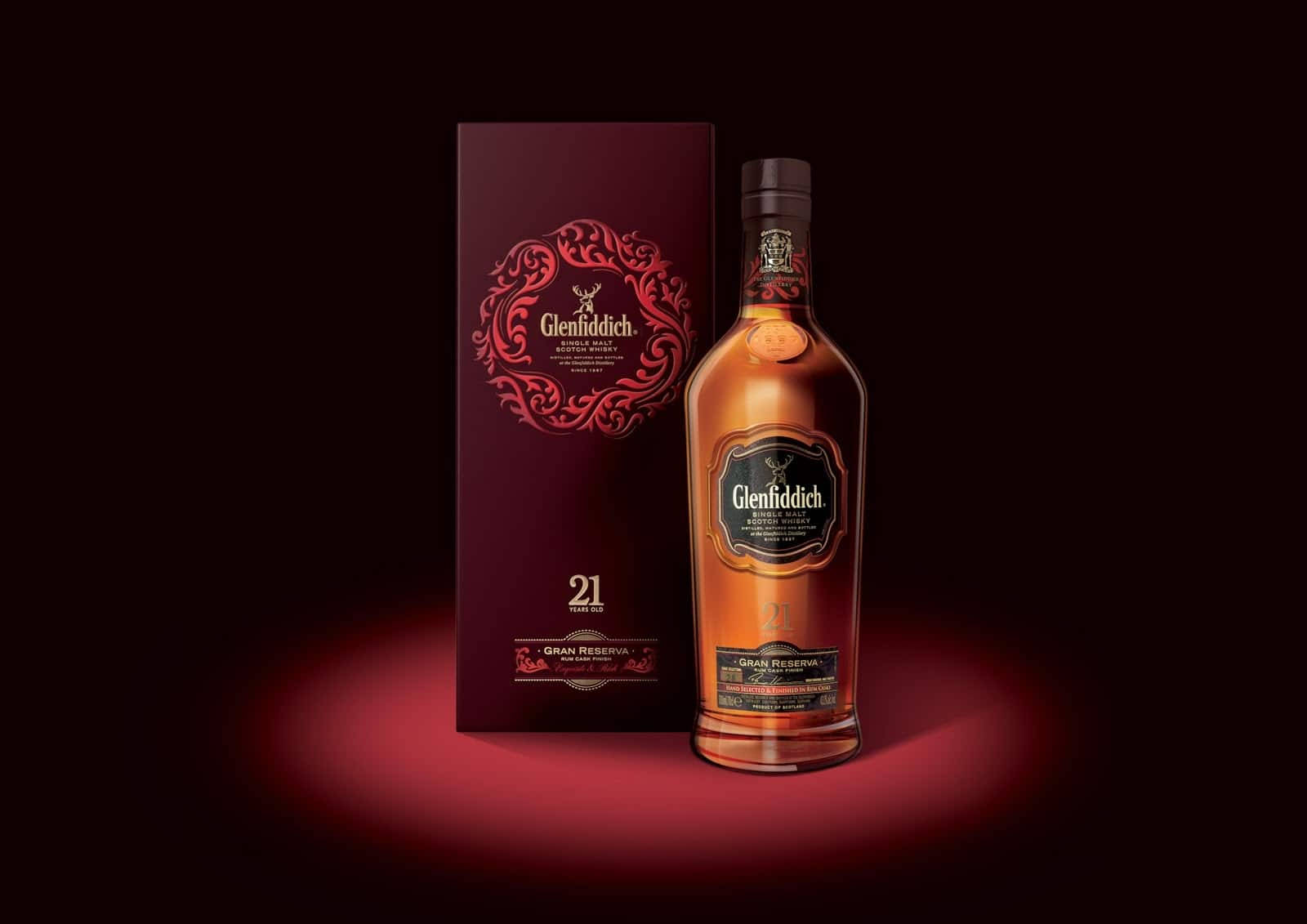 alcohol 桌布 壁紙 — 一瓶 Glenfiddich 21 年威士忌在黑暗背景下，在其華麗的紅色盒子旁邊溫暖地發光。