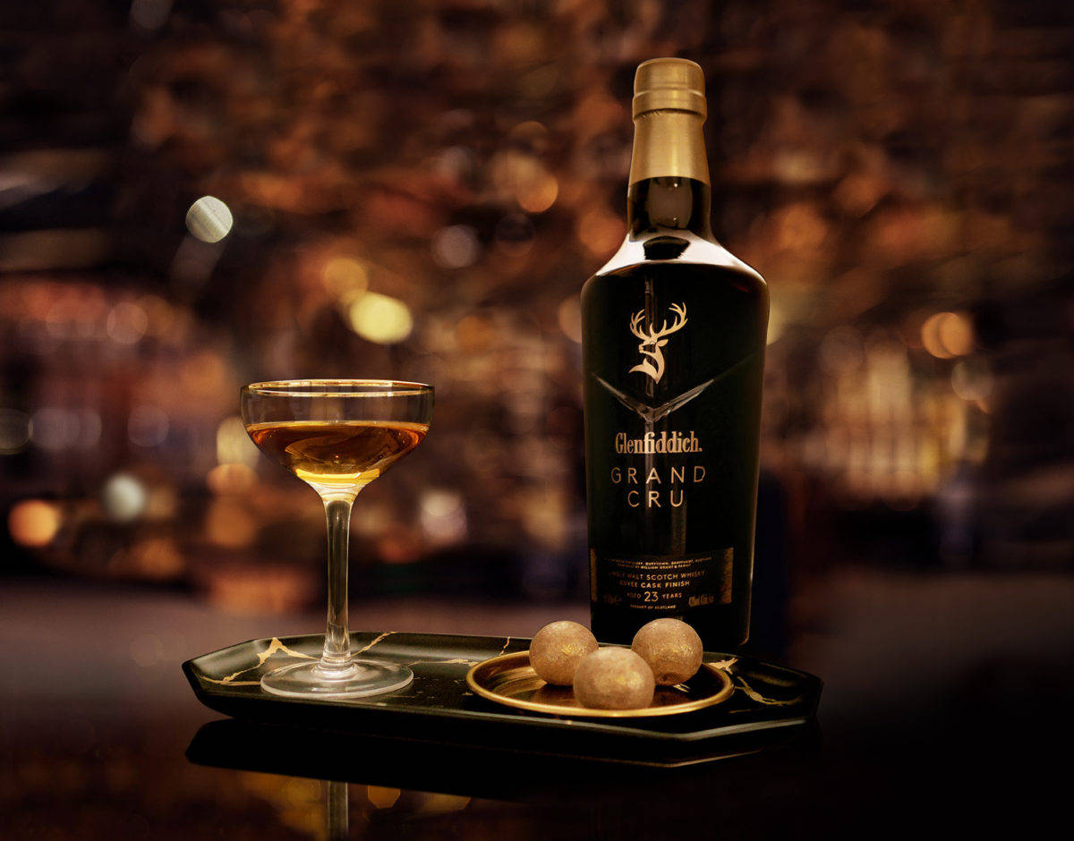 alcohol 桌布 壁紙 — 一瓶 Glenfiddich Grand Cru 威士忌和一個裝滿雞尾酒的酒杯優雅地放在托盤上，配以冰球，背景是溫暖照明的酒吧。